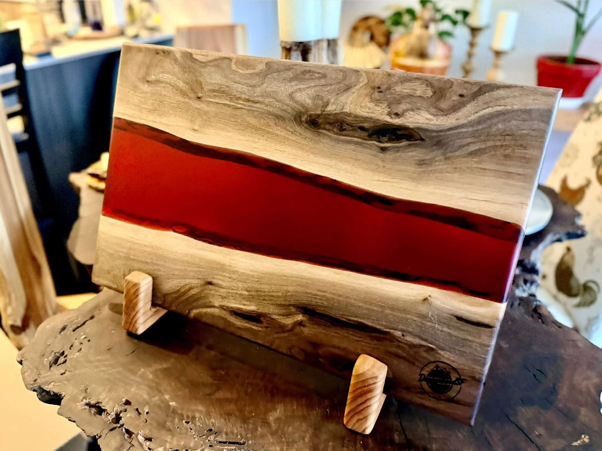 Wooden art piece with a horizontal red resin inlay, supported by two small wooden stands, on a textured wooden surface.