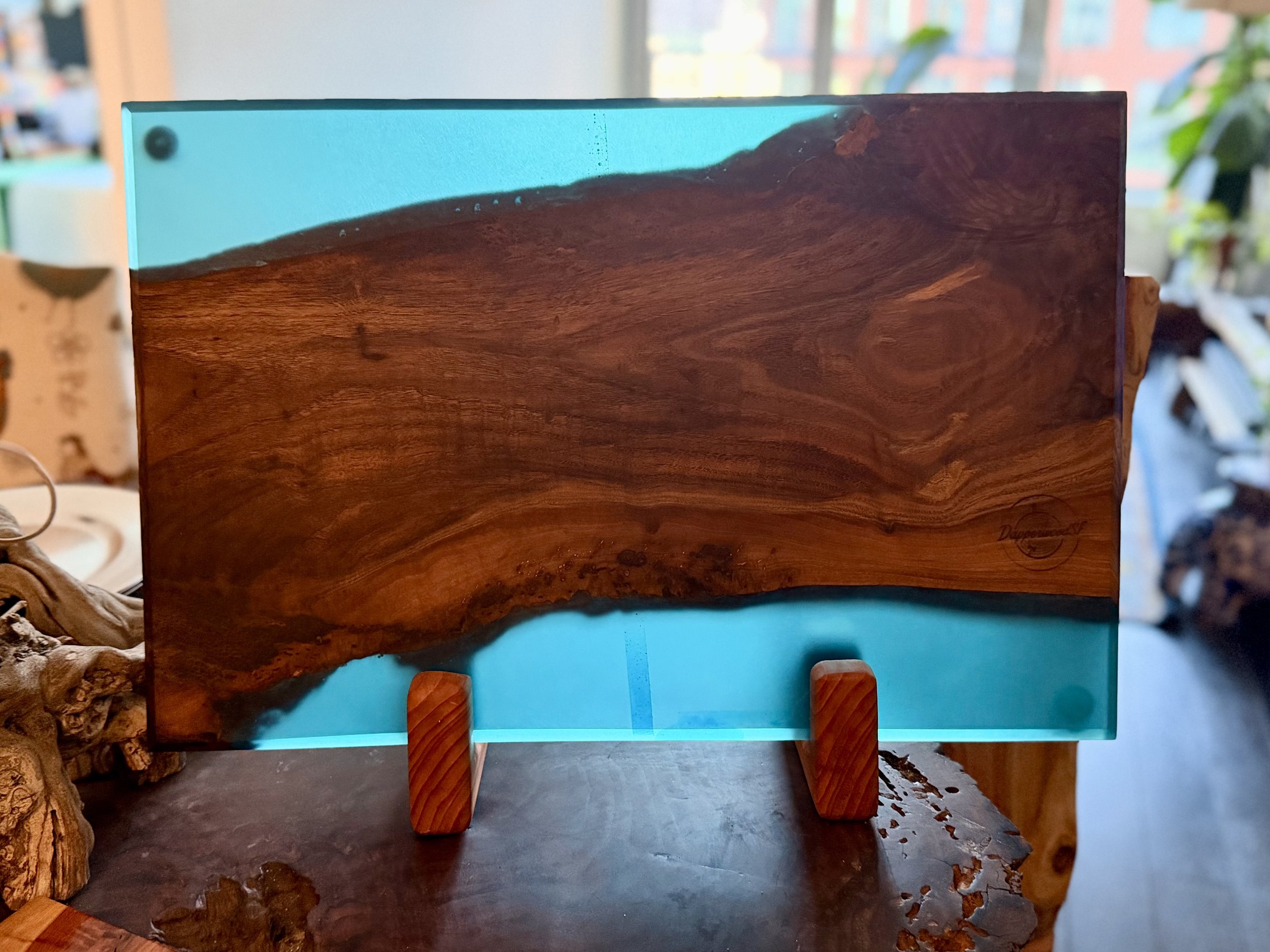 A decorative glass and wood display with a wood panel placed on a wooden stand, showcasing a large wood grain pattern with a blue translucent glass section at the bottom.