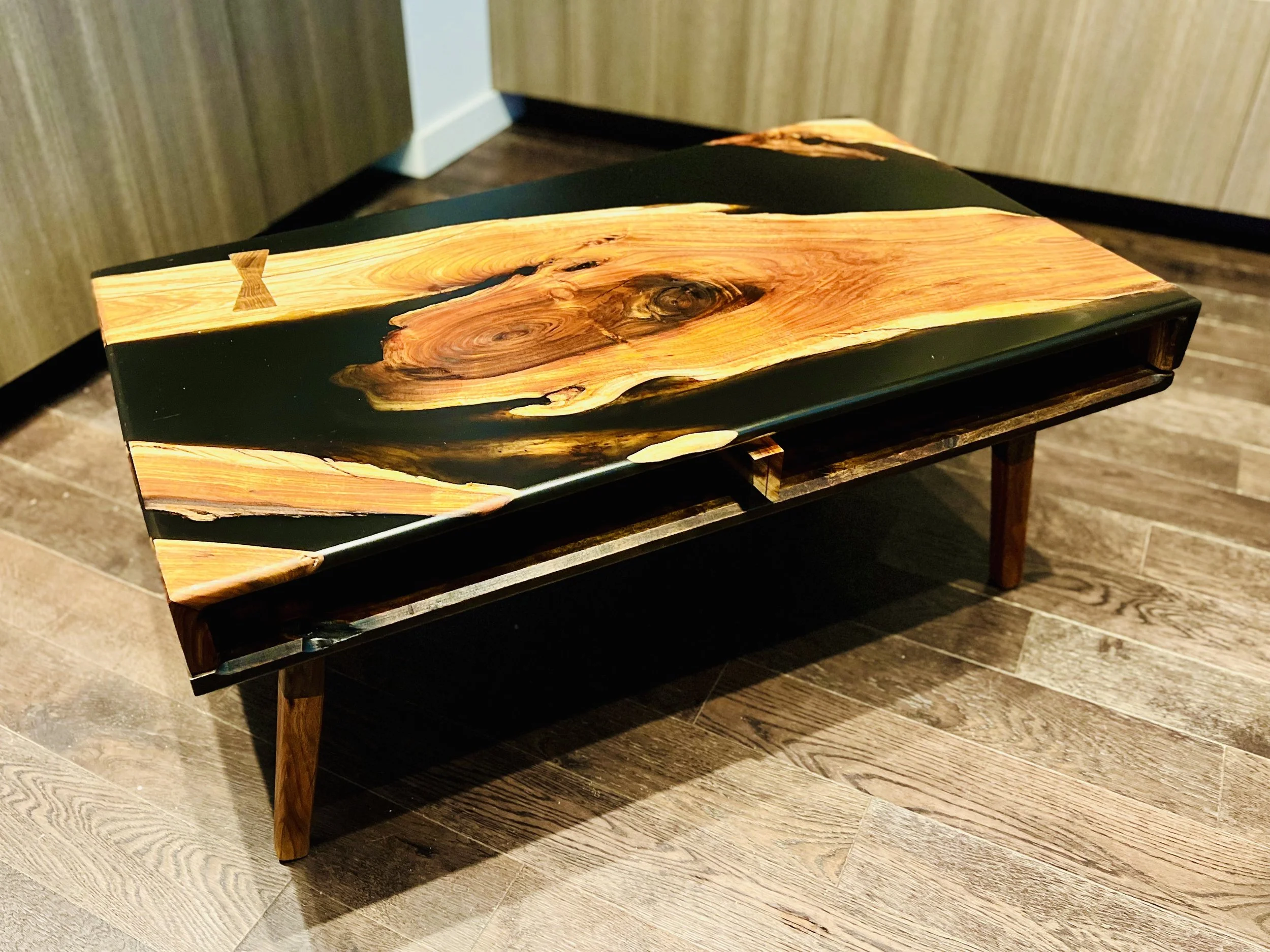 Wooden table with a polished surface featuring natural wood grain patterns, placed on a wooden floor in a room with wood-paneled walls.