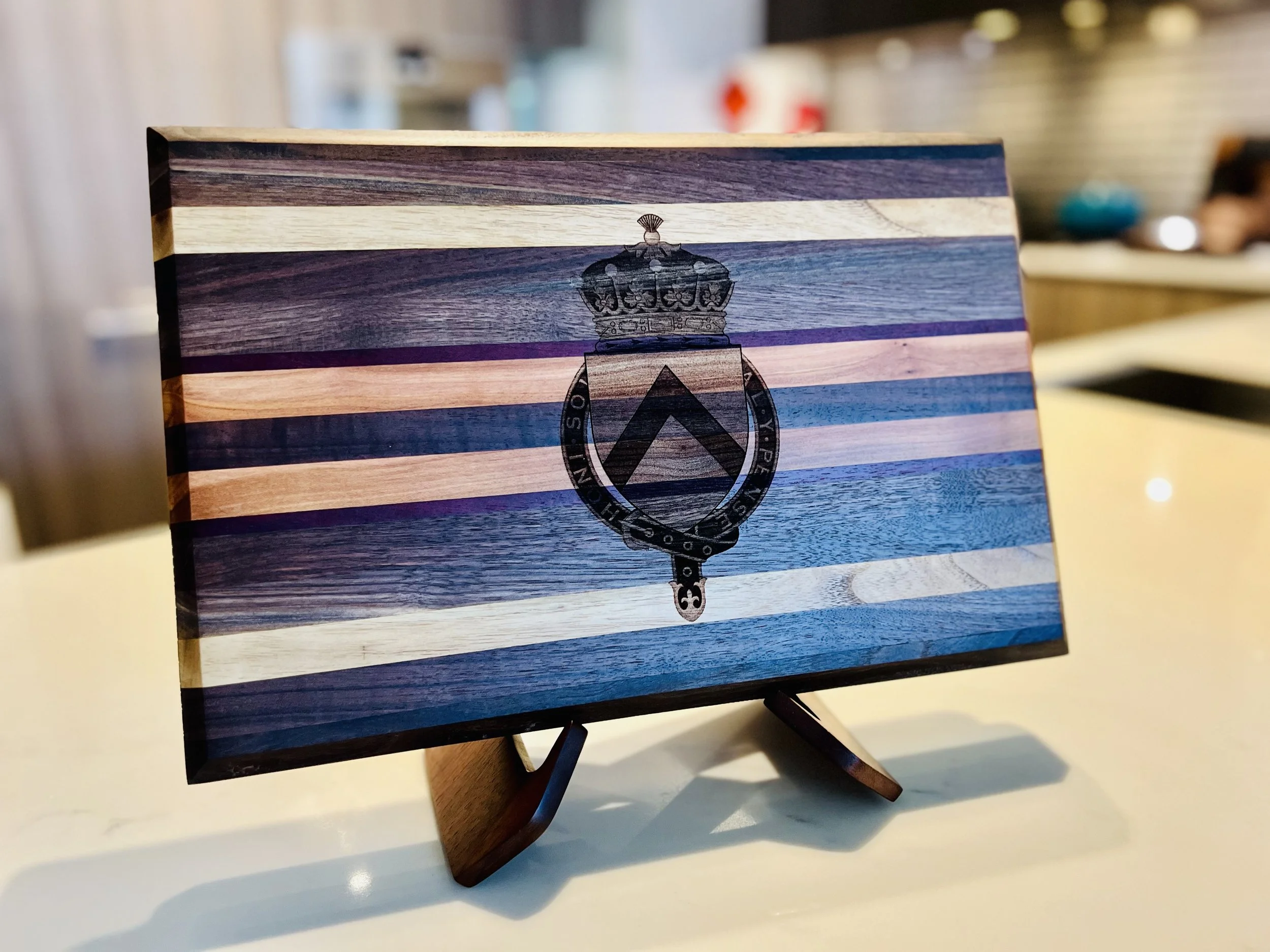 A wooden stand with a horizontal striped wood pattern background featuring shades of brown, blue, purple, and cream, with a black emblem of a crown and shield in the center.