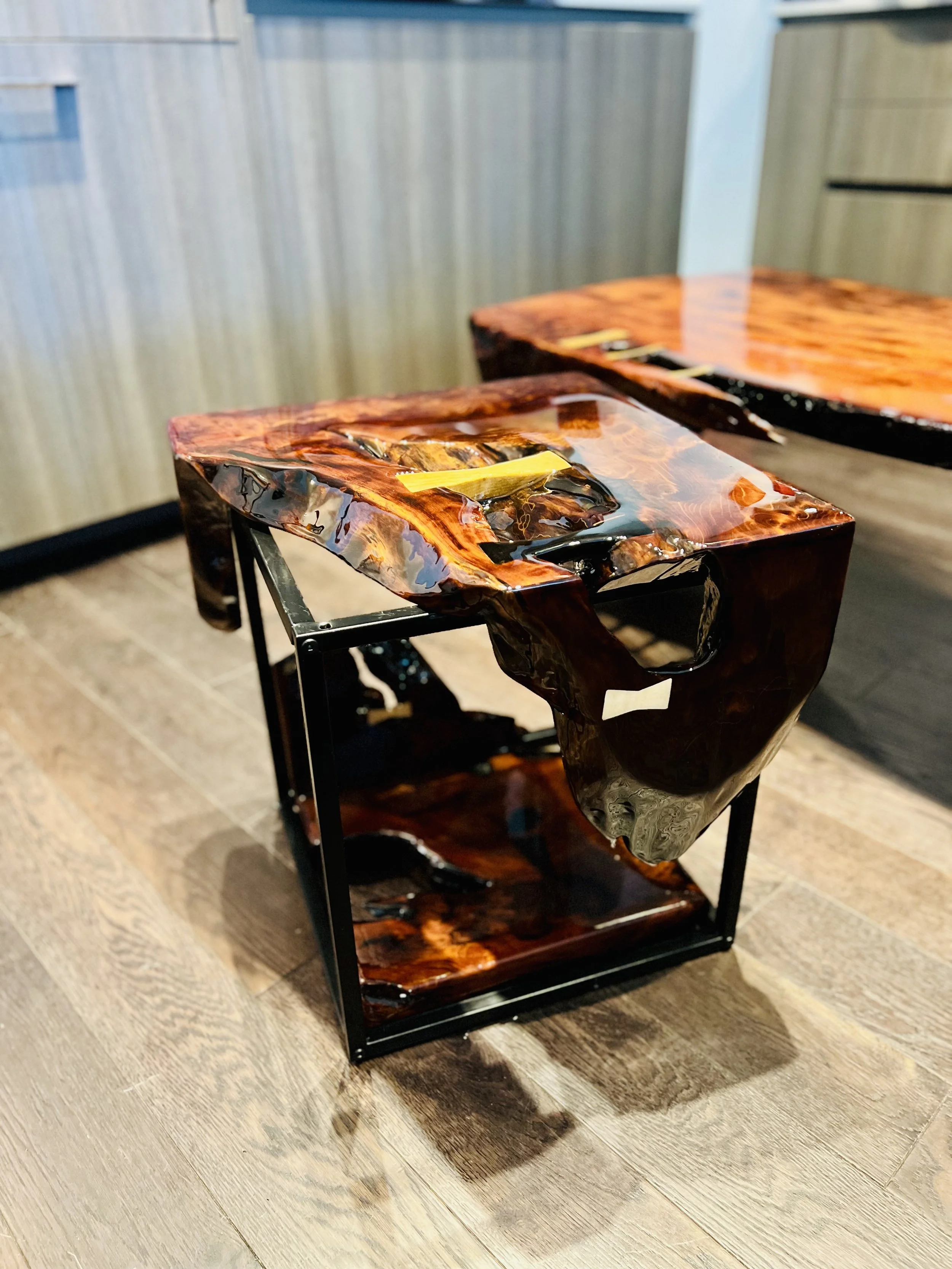 A decorative wooden side table with a glossy finish and a metal frame, placed on a wooden floor in a room with wood-paneled walls.