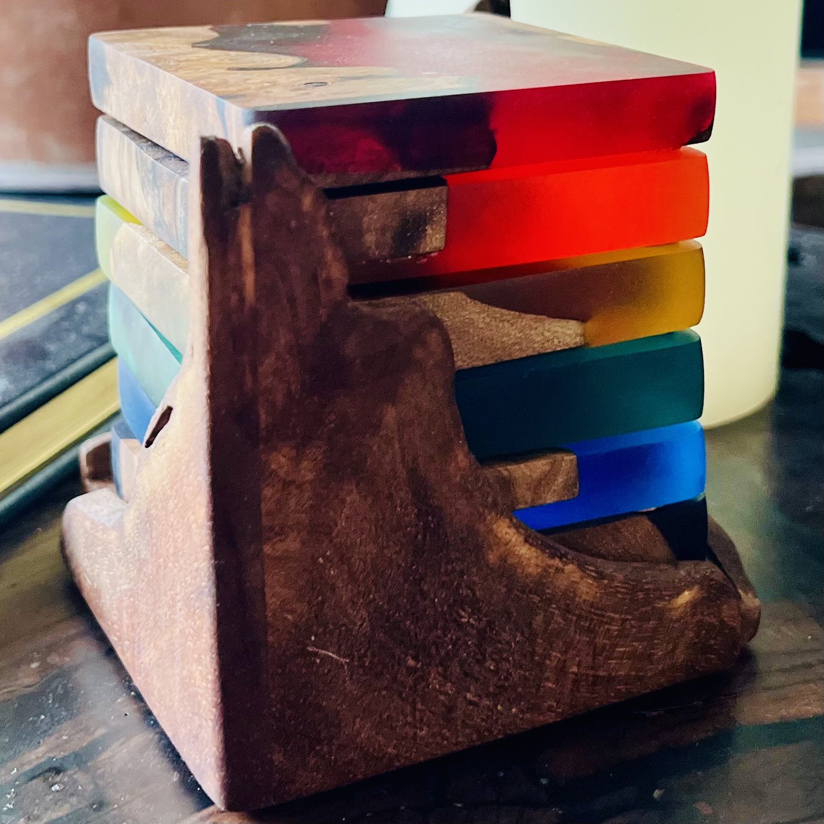 Wooden coasters with colorful horizontal blocks stacked on top of a carved wooden coaster holder.