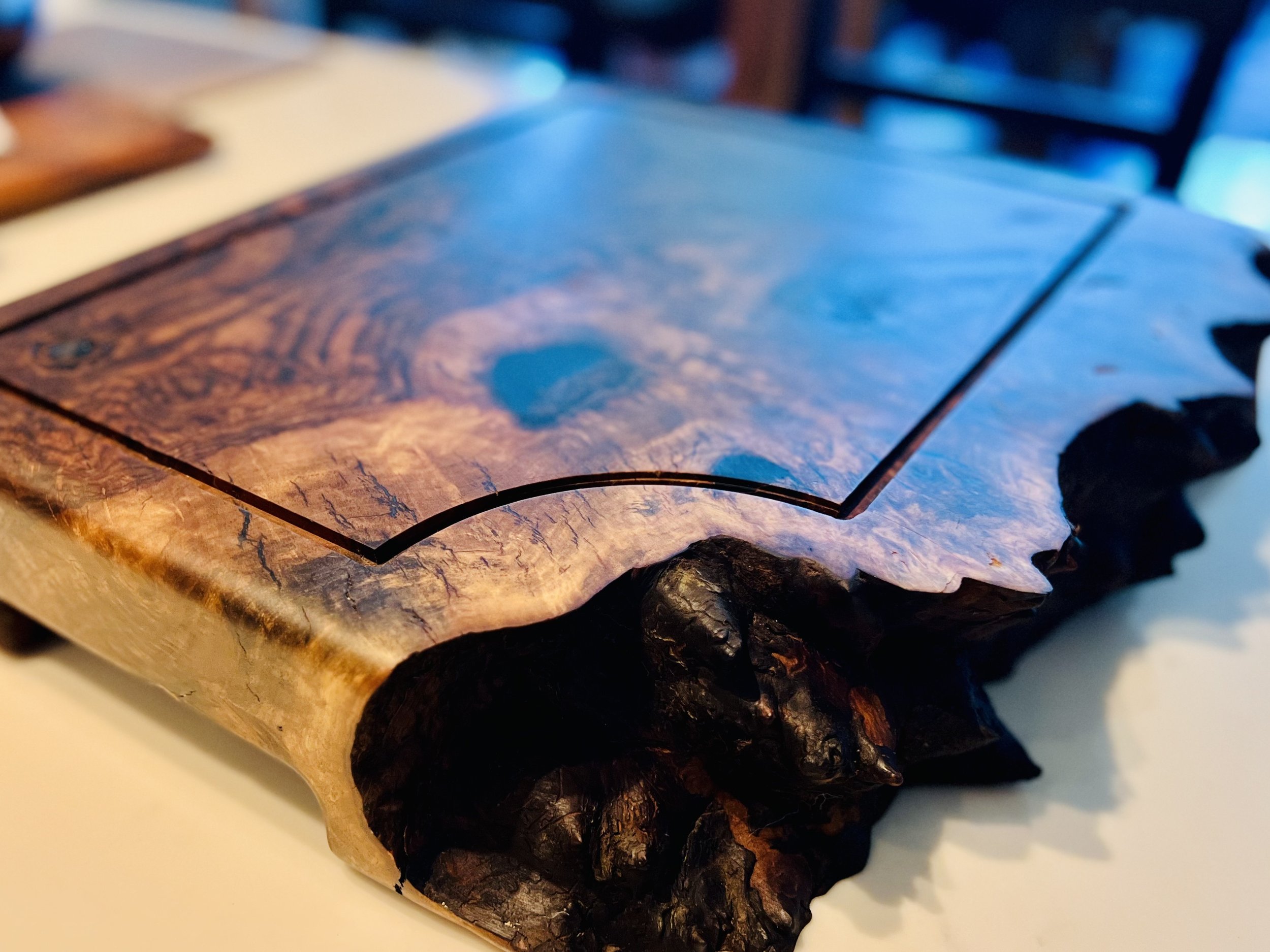 Close-up of a wooden cutting board with a natural edge, on a white countertop.