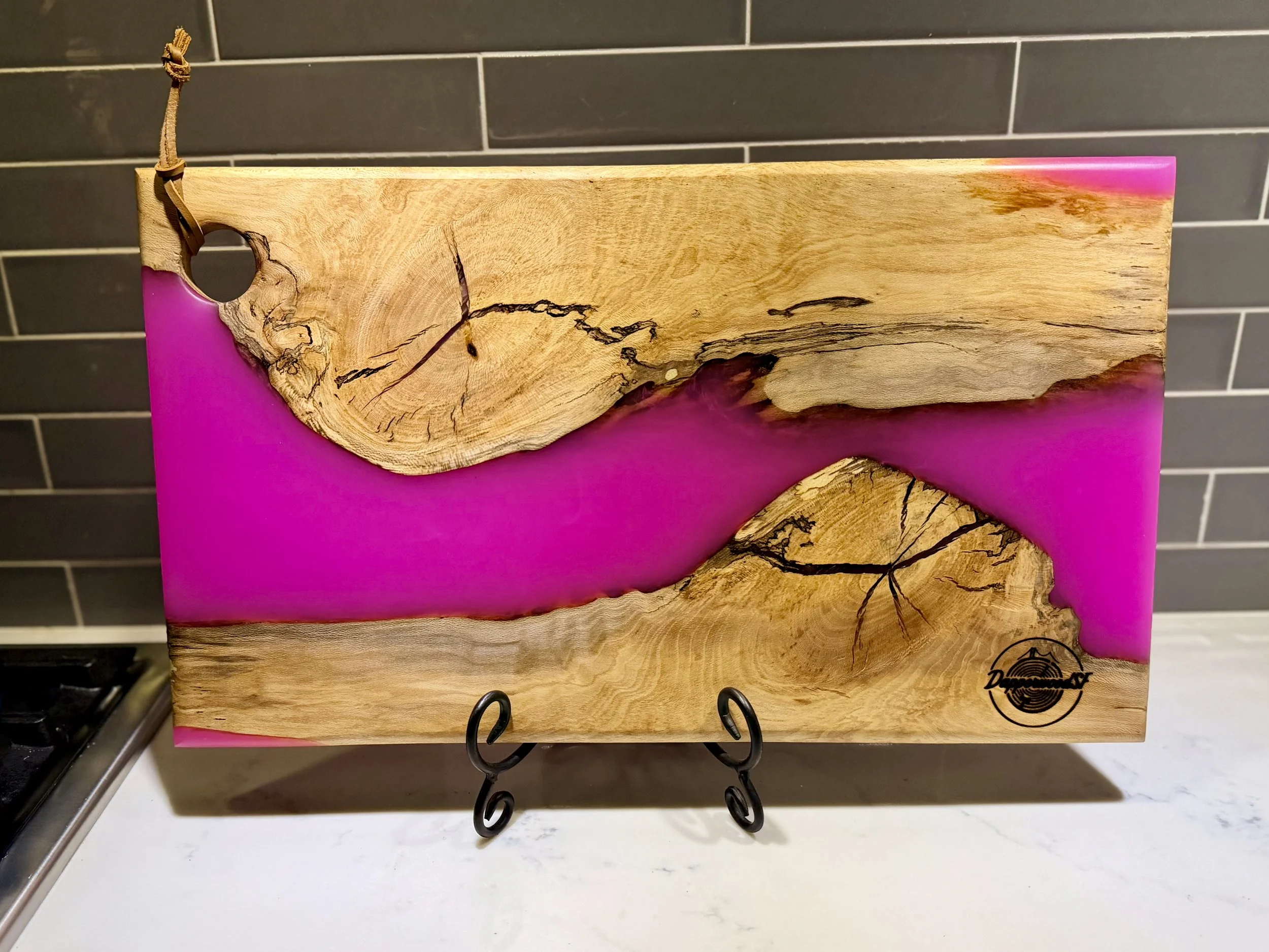 Wood and pink resin decorative art piece on display on a stand, featuring natural wood grain and pink resin background against a dark tiled wall.