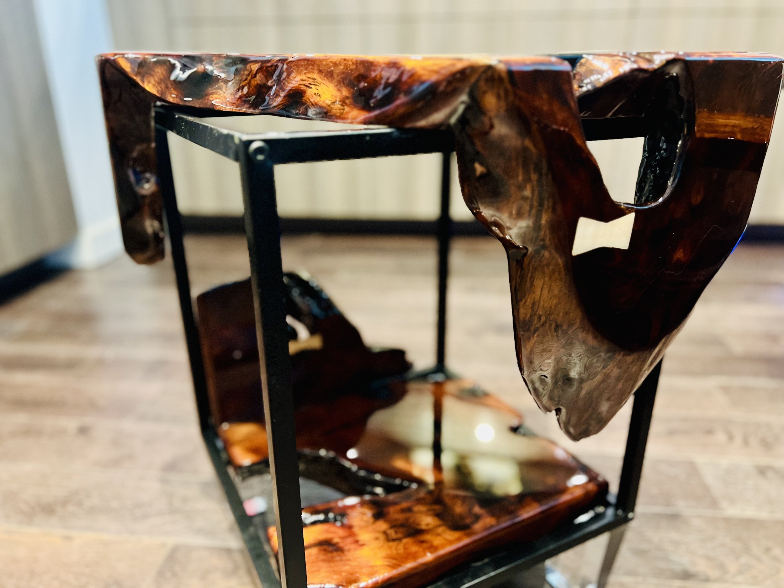 A unique coffee table with a black metal frame and a top, middle, and bottom shelf made of polished, irregularly shaped wood with a rich, dark finish.