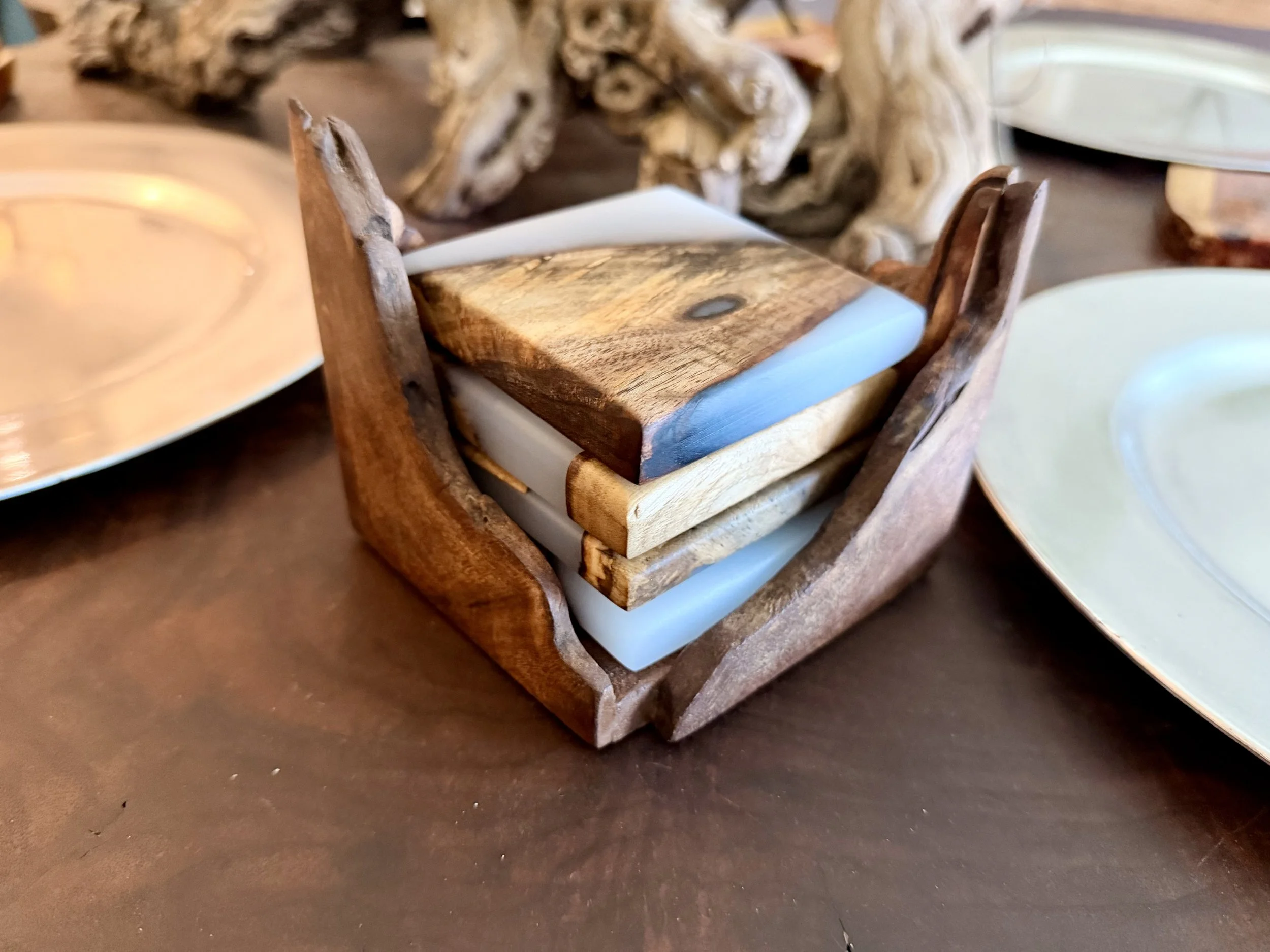 Stack of colored wood and resin coasters inside a wooden holder on a table.