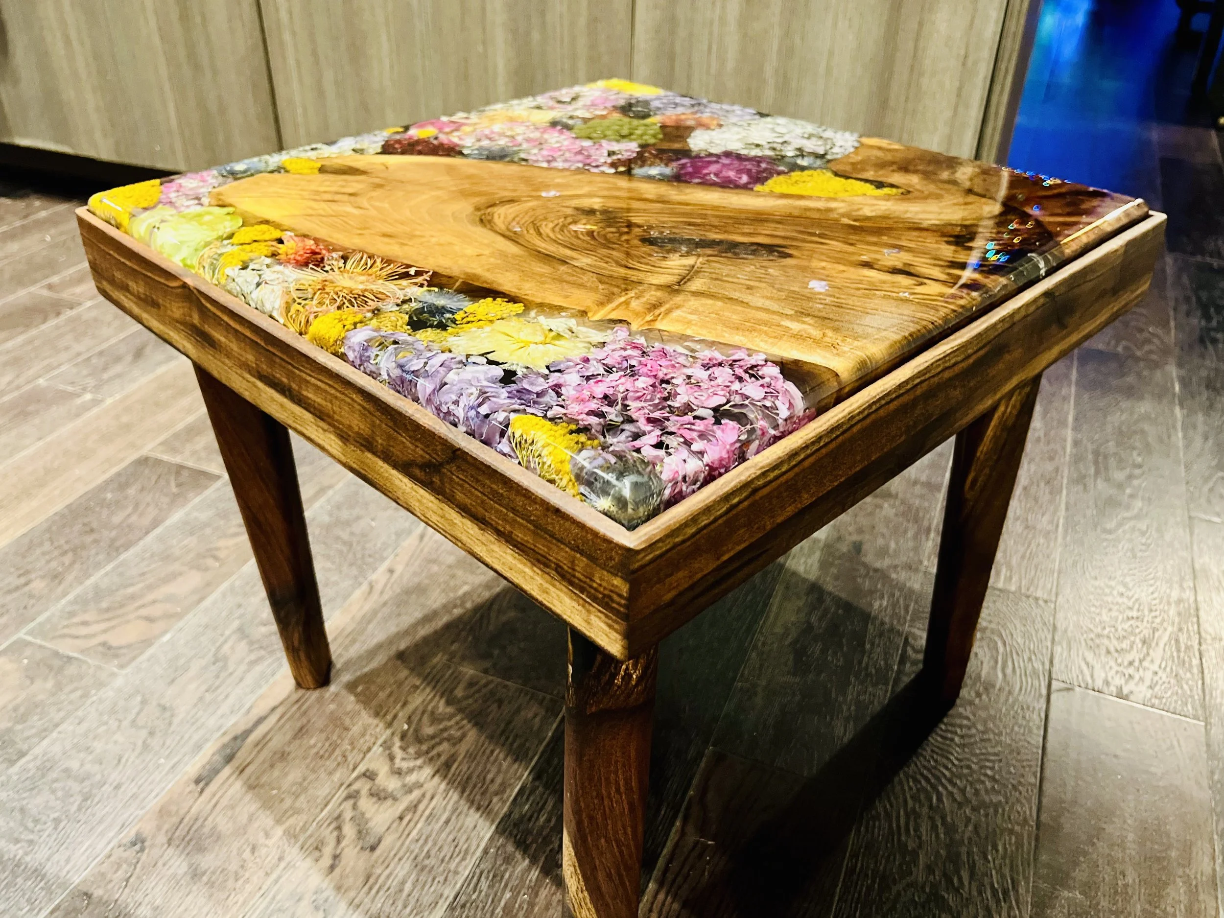 A wooden table with vibrant and colorful flowers cast in epoxy resin.