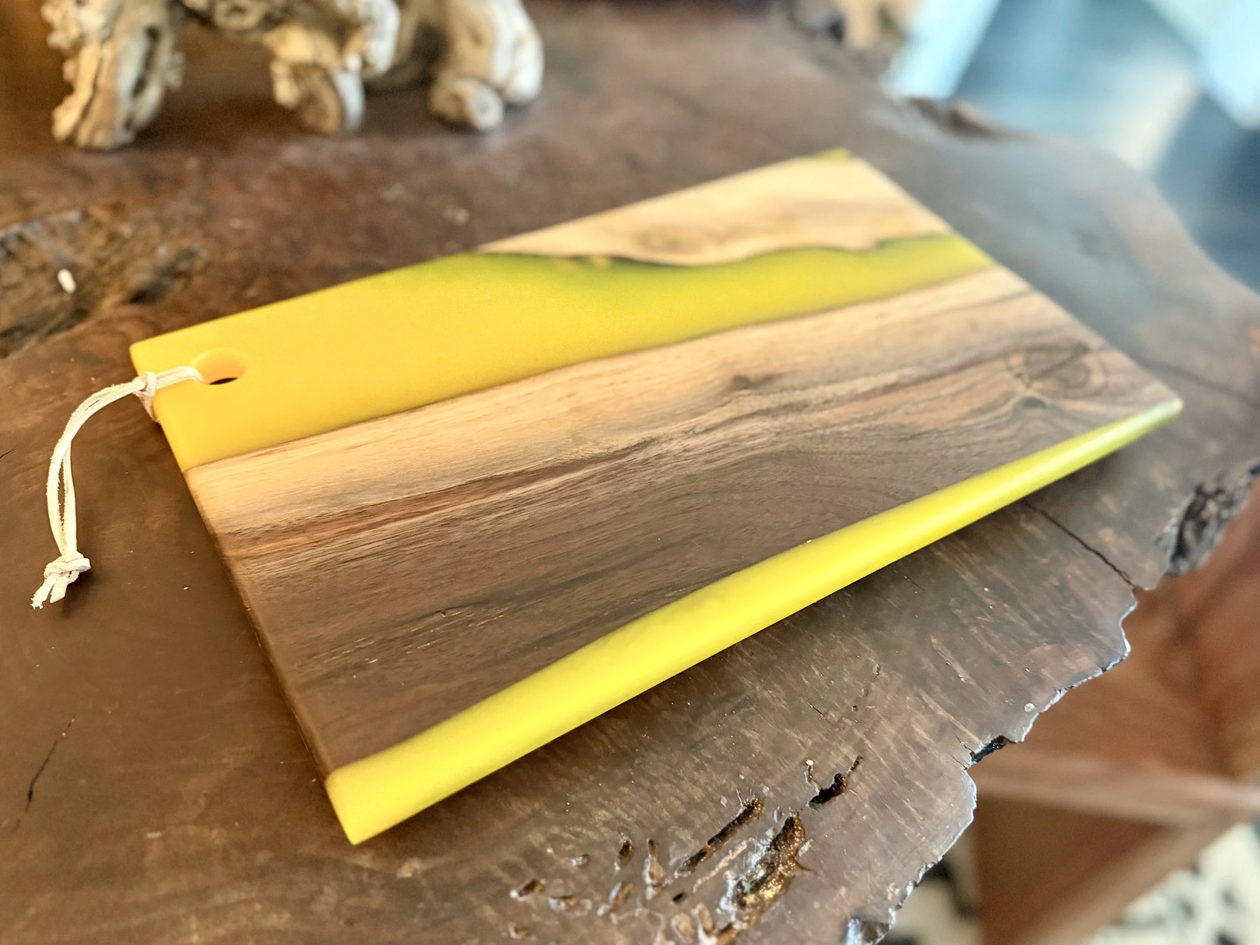 A rectangular wooden chopping board with yellow accents and a decorative yellow strip along the edge, placed on a rustic wooden surface.