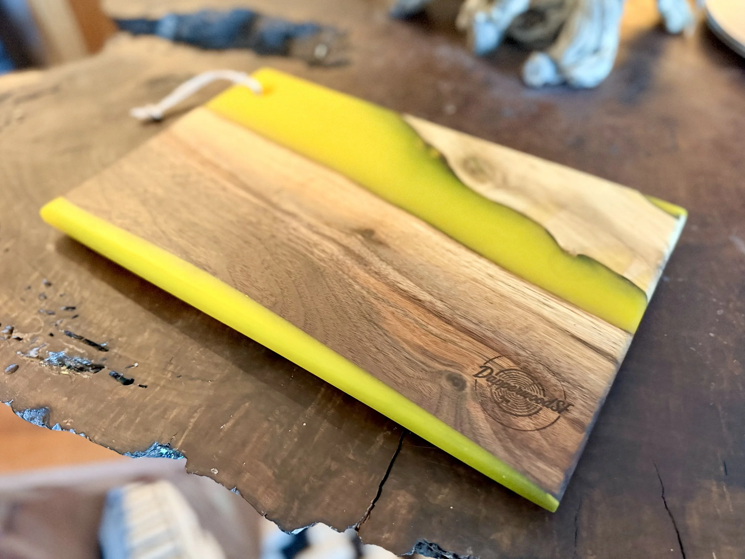 A cutting board made of wood and yellow resin, placed on a wooden table.