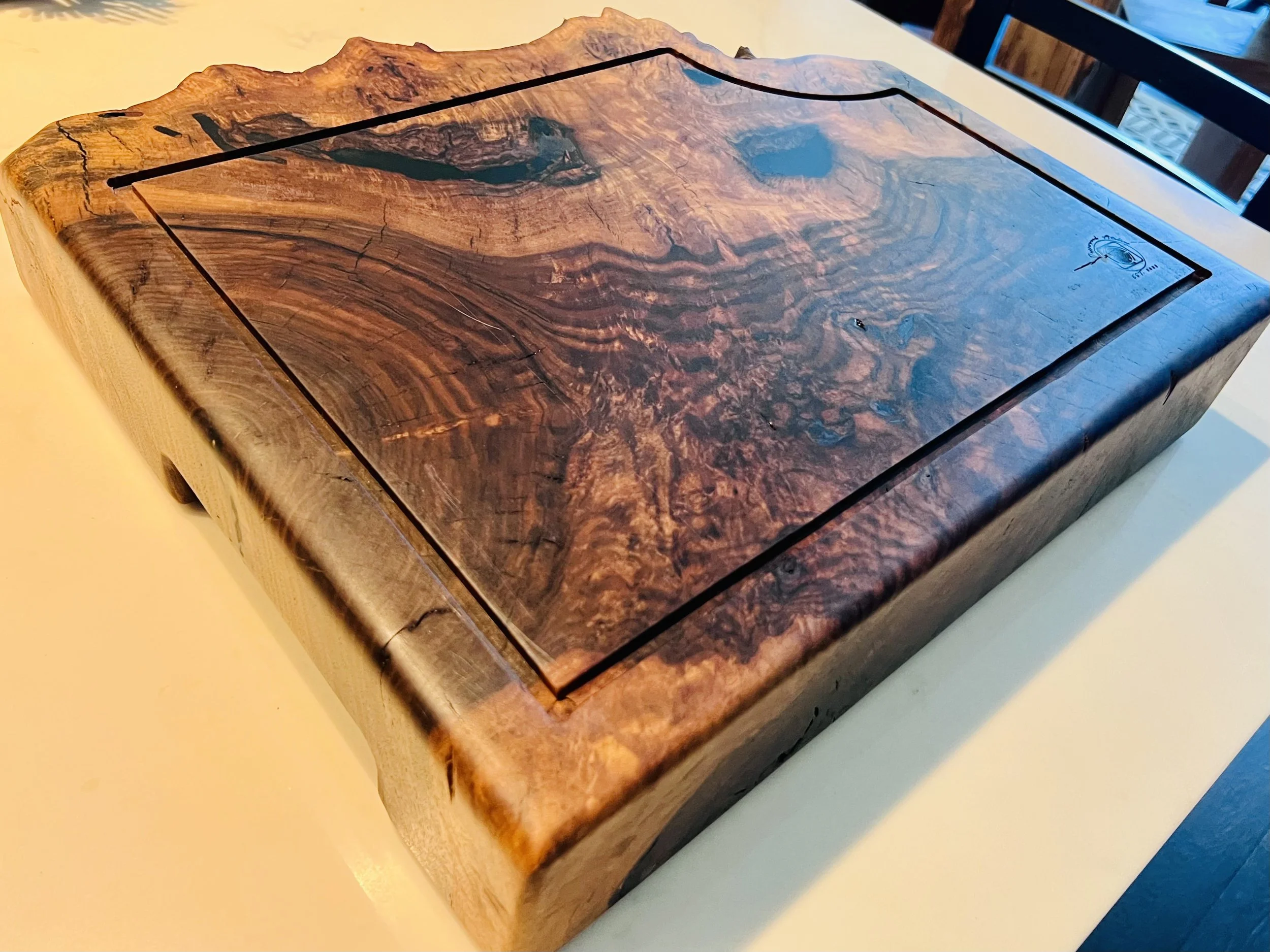 A wooden cutting board with a rectangular shape, featuring a natural, rough edge on one side and a smooth, polished surface with a wood grain pattern in shades of brown.