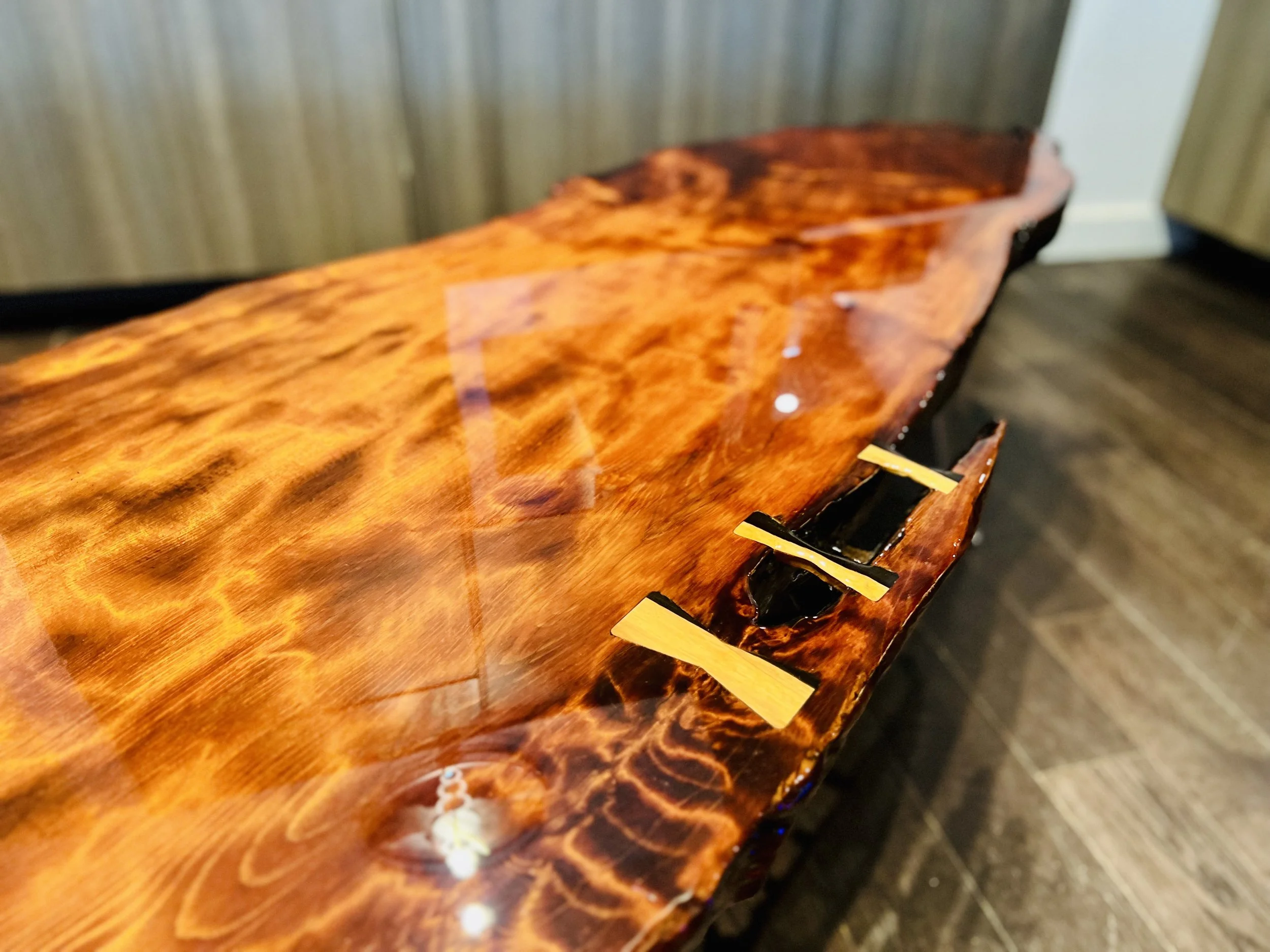 Close-up of a polished, dark wood table with yellow protective strips on the edges and a small section of irregular edge visible.