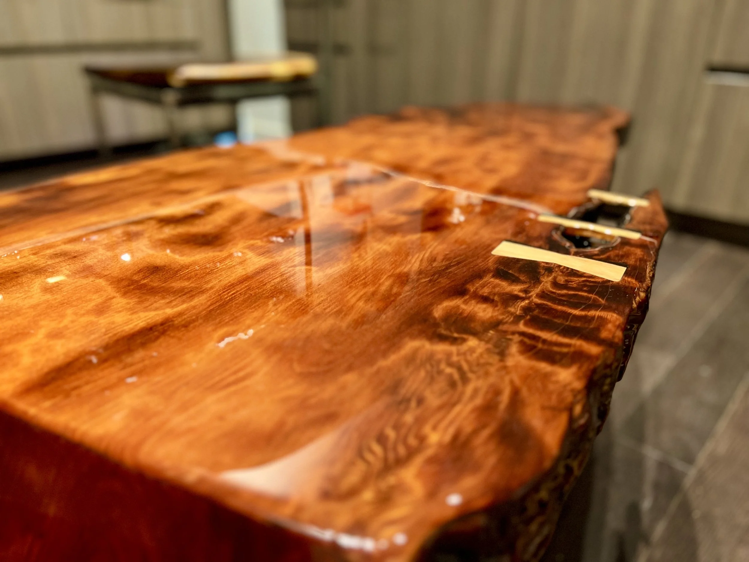 Close-up of a polished, glossy wooden table with a natural edge in a rustic setting.
