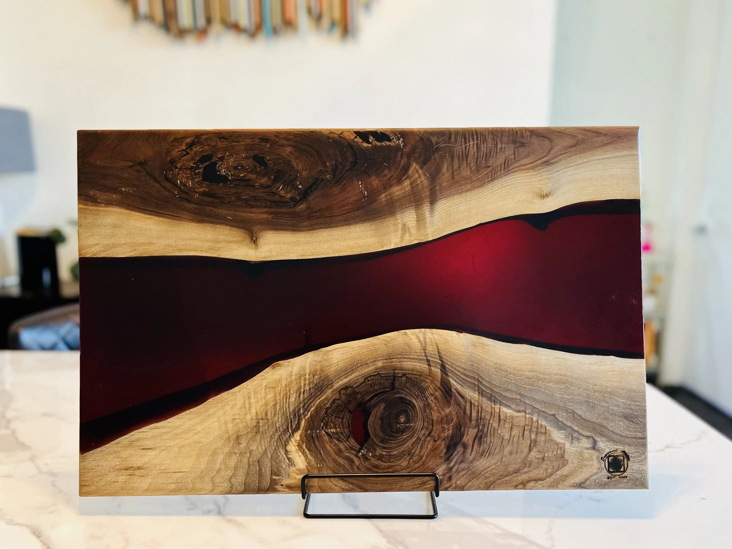A wooden art piece with natural wood grain and knots, with a black and red abstract stripe running horizontally across the center, displayed on a black stand.