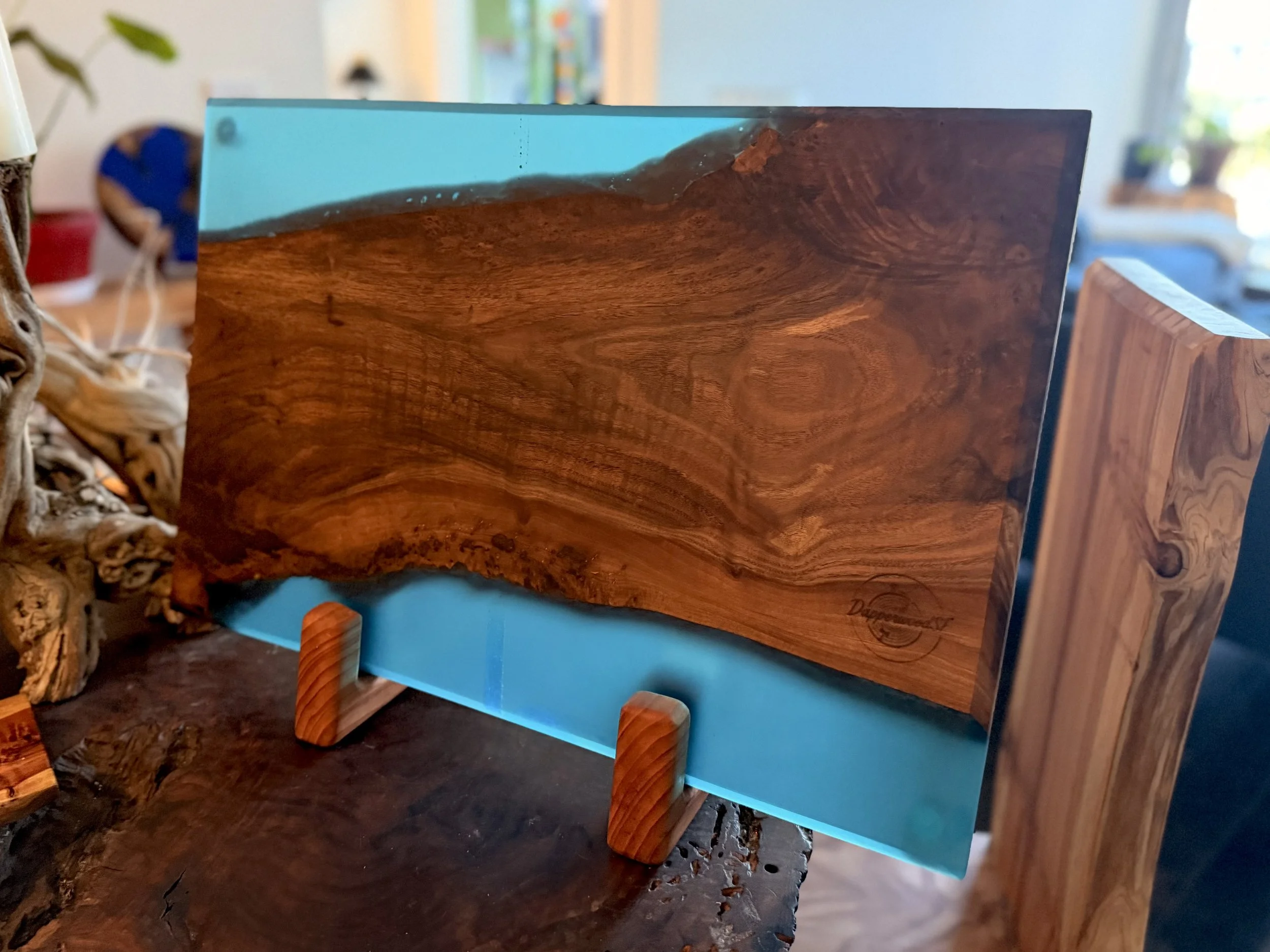 A piece of wood framed with a glass panel, mounted on small wooden supports, with a signature or mark at the bottom right corner, placed on a wooden surface.