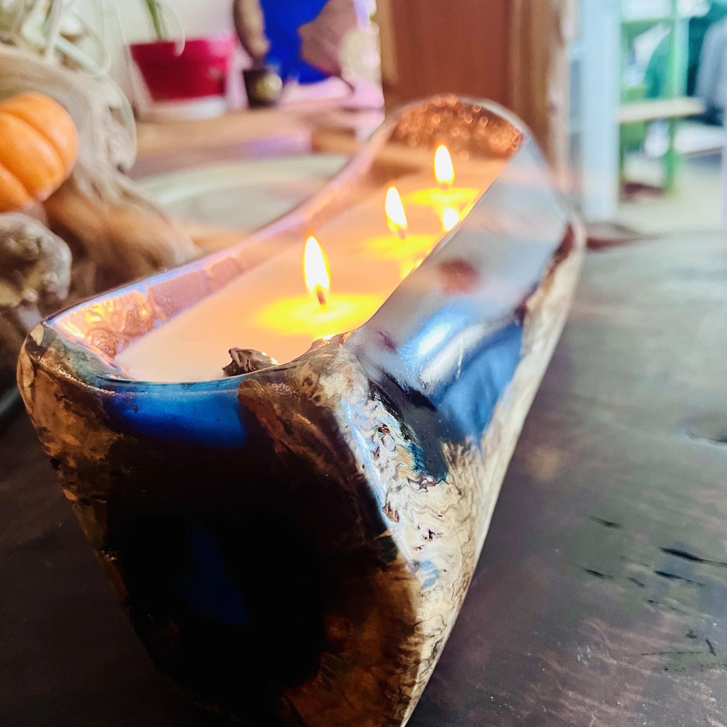 A rectangular candle holder with three lit candles, made of wood with a polished, marble-like appearance, placed on a dark wooden surface.