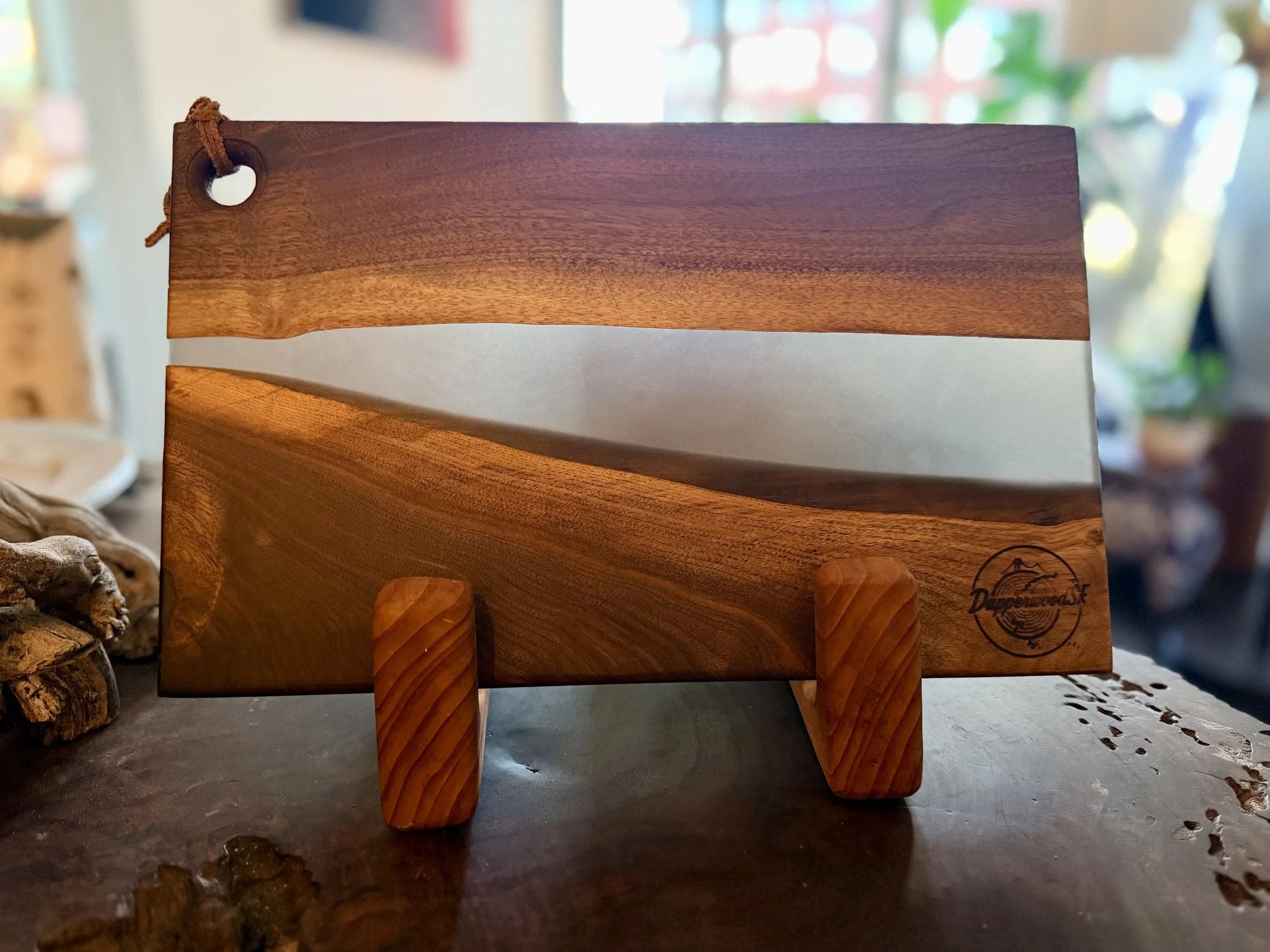 A wooden sign with a landscape design, propped on two small angled wooden supports, with a logo in the lower right corner that reads 'Dune Made Inc.'.