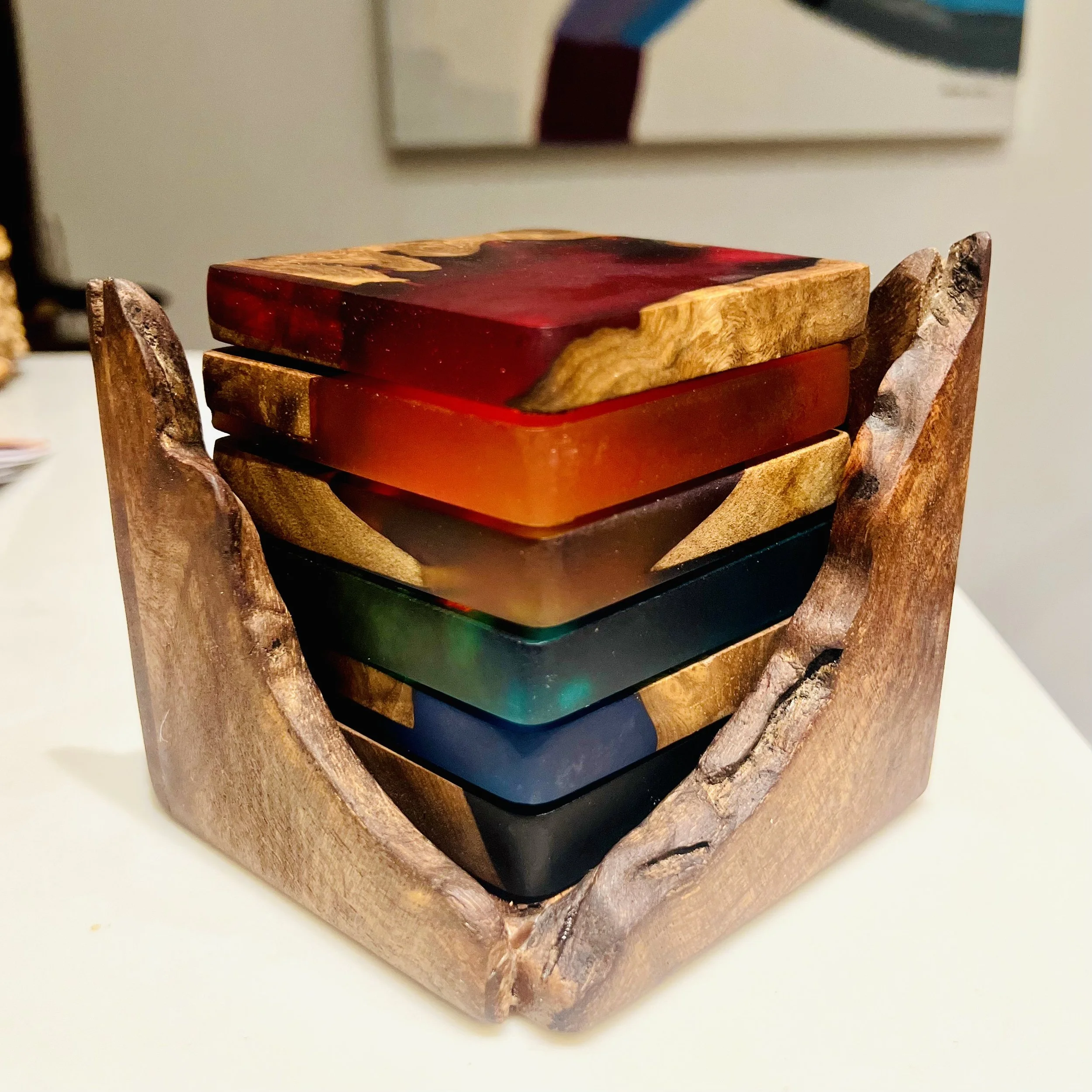 A wooden holder containing several colorful resin coasters stacked inside.