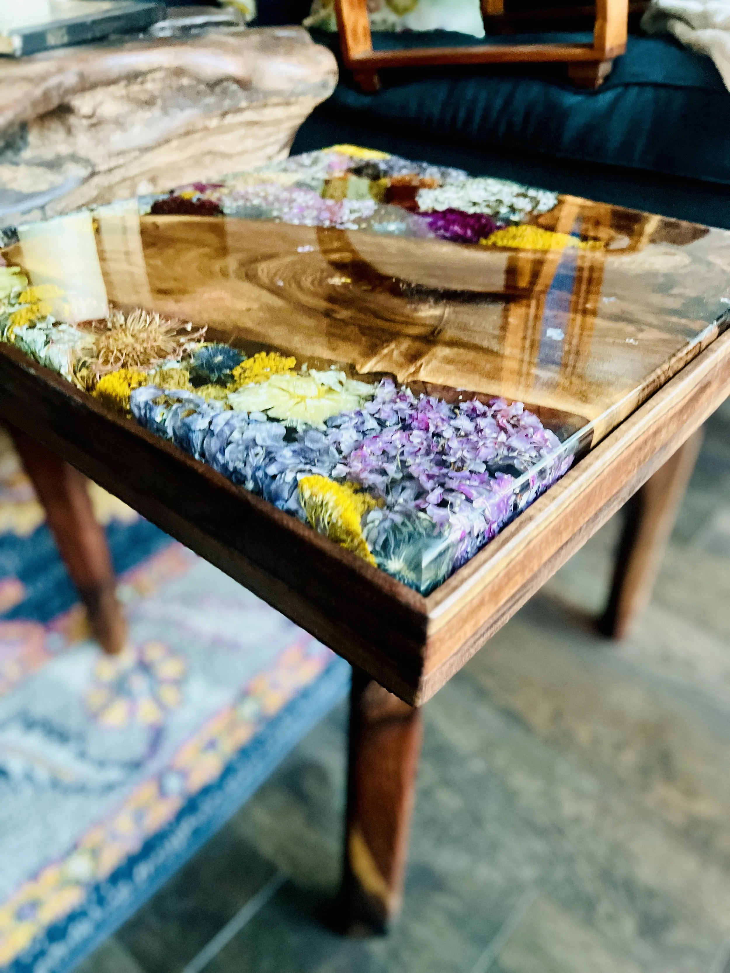 Close-up of a wooden table with a glass cover decorated with colorful pressed flowers inside.