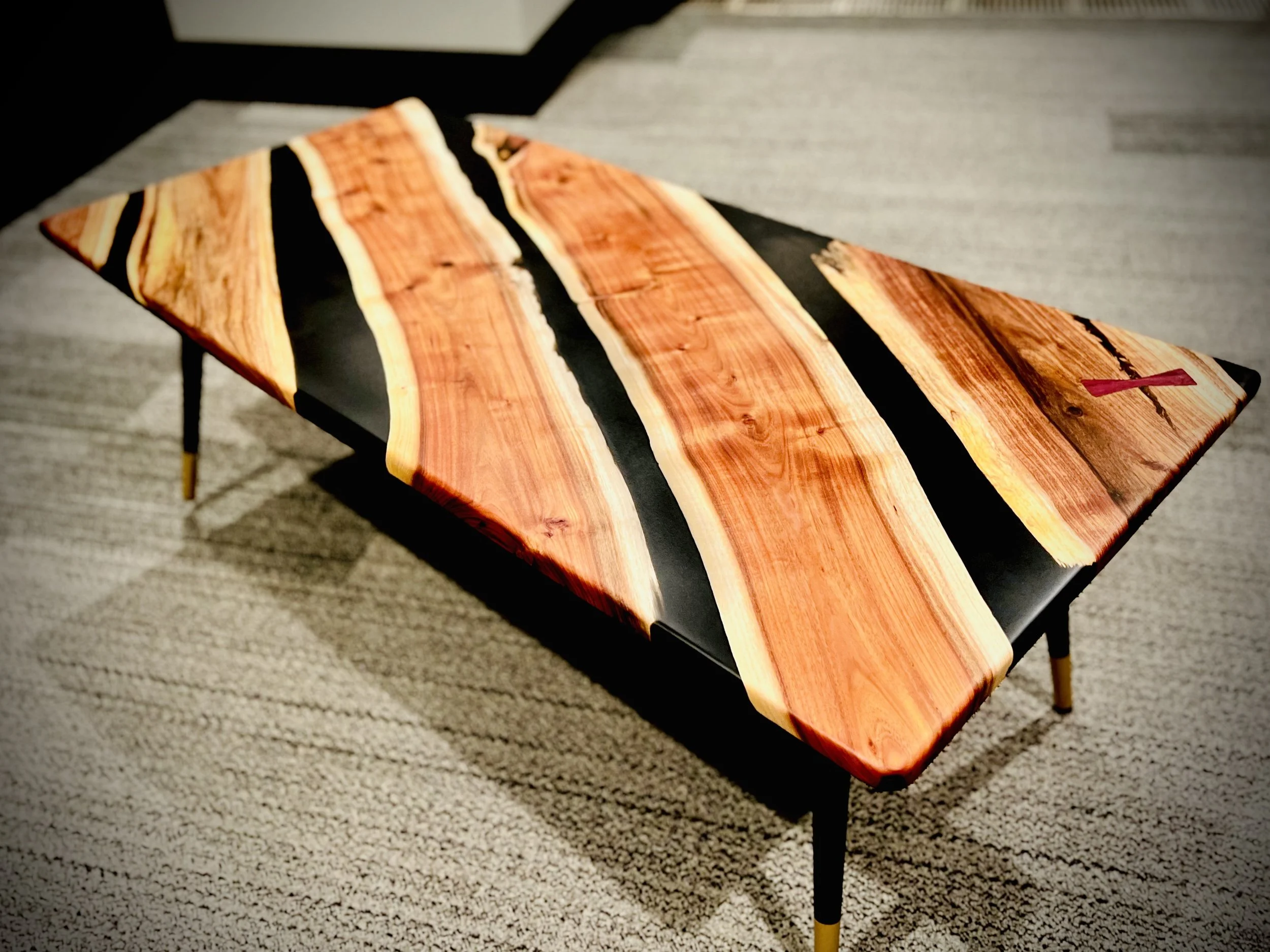 A rectangular coffee table with a glossy black surface and a wood top featuring natural wood grain and black inlays, placed on a carpeted floor.