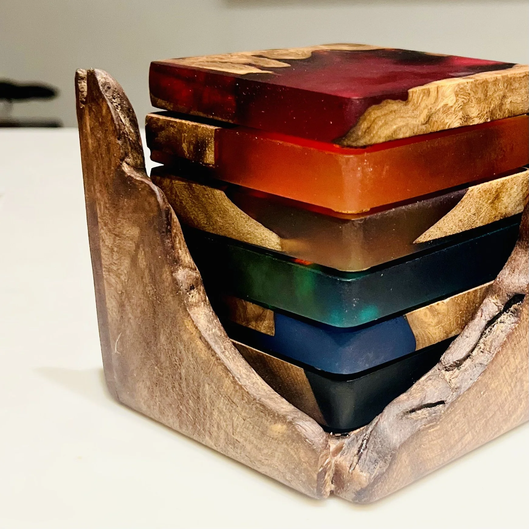Stack of colorful resin coasters in a wooden holder.