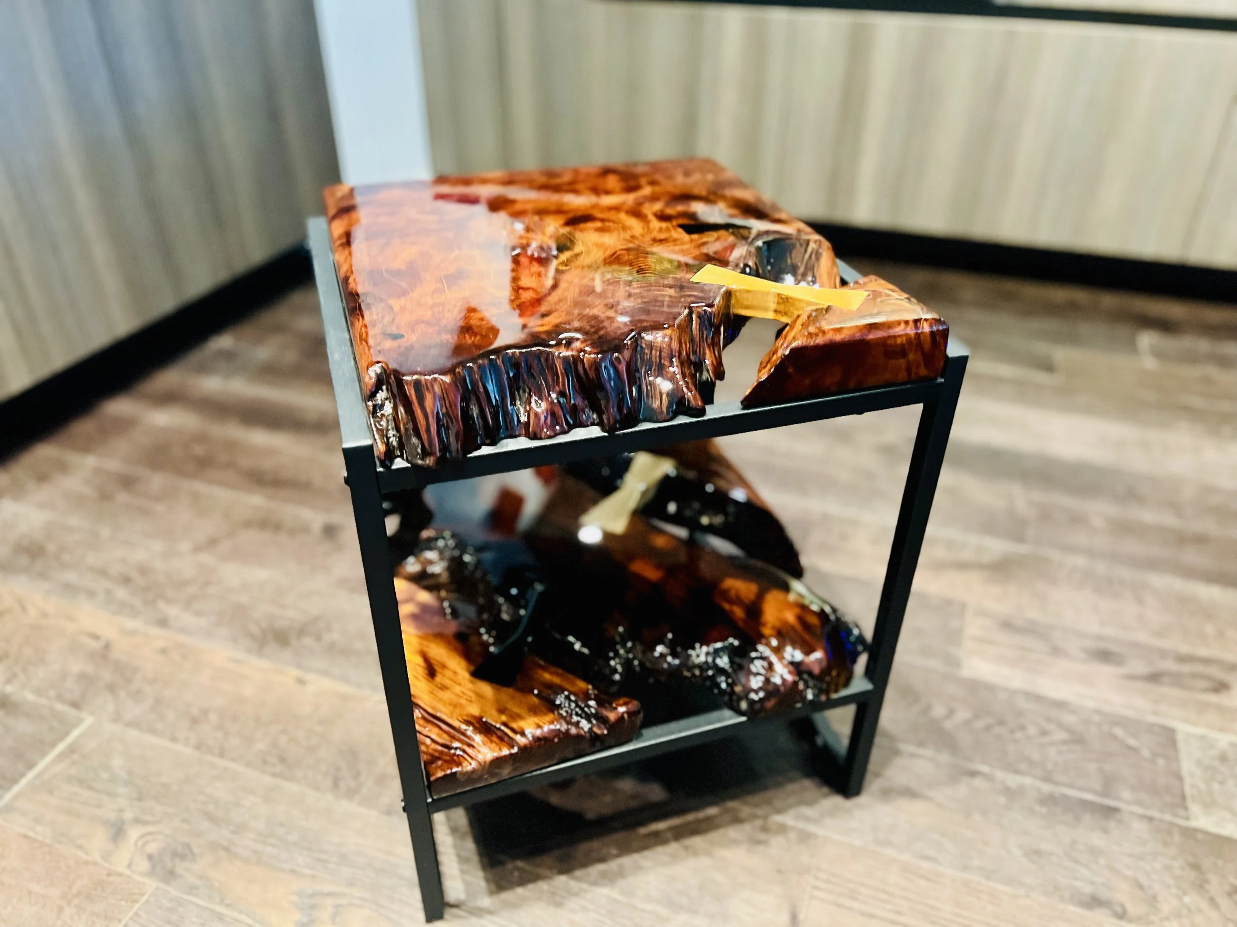 A three-tiered display stand coffee table showcasing polished, glossy, amber-colored wood with a natural, irregular edge design on each shelf.