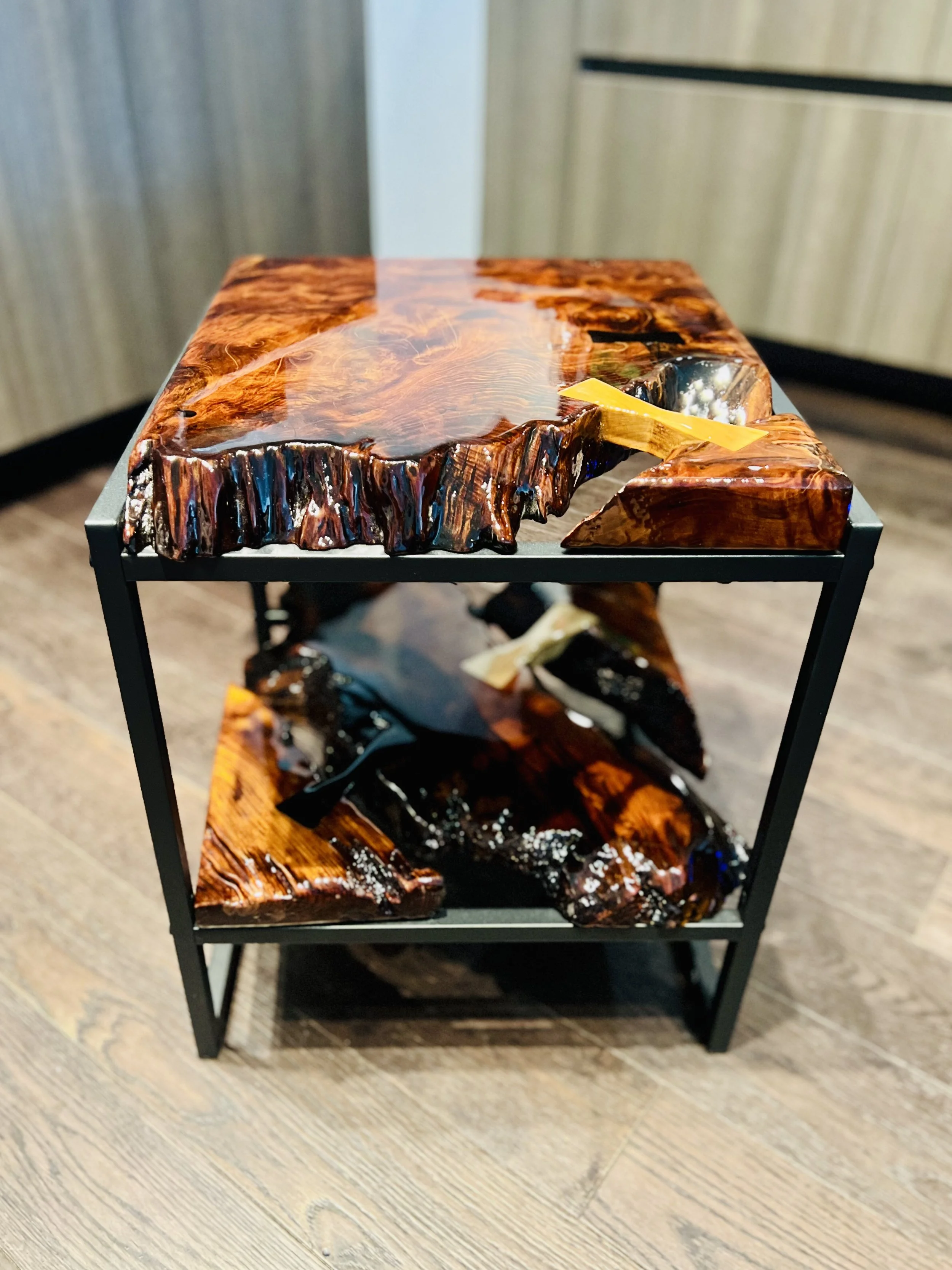 A two-tiered table with a frame made of black metal and wooden slabs with a glossy, polished finish and rich, warm tones, displaying natural wood grain patterns.