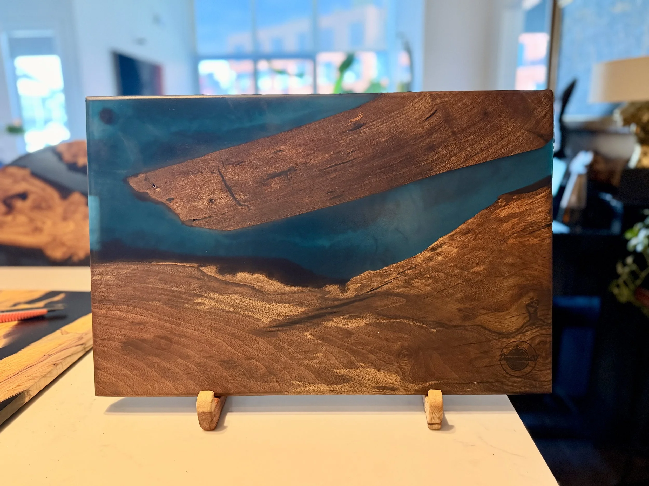 Wooden art piece with epoxy blue resin, mounted on small wooden stands, displayed on a white surface in a store.
