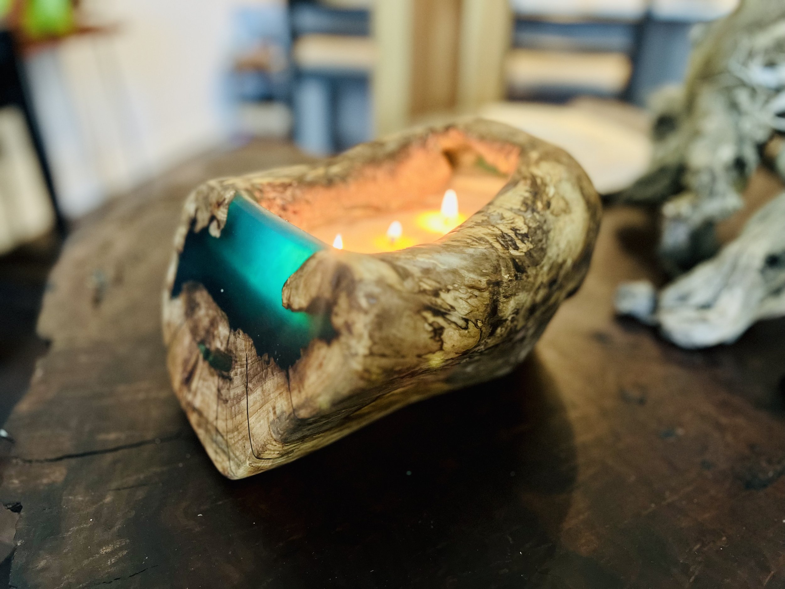 A candle in a hollowed-out piece of wood with lit flames on a dark wooden table.