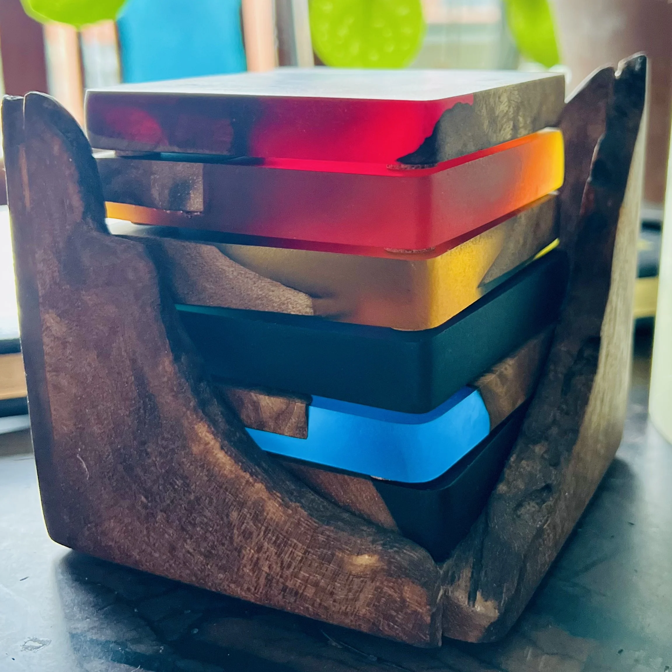A wooden coaster set with colorful epoxy pieces stacked inside each other on a wooden coaster holder.