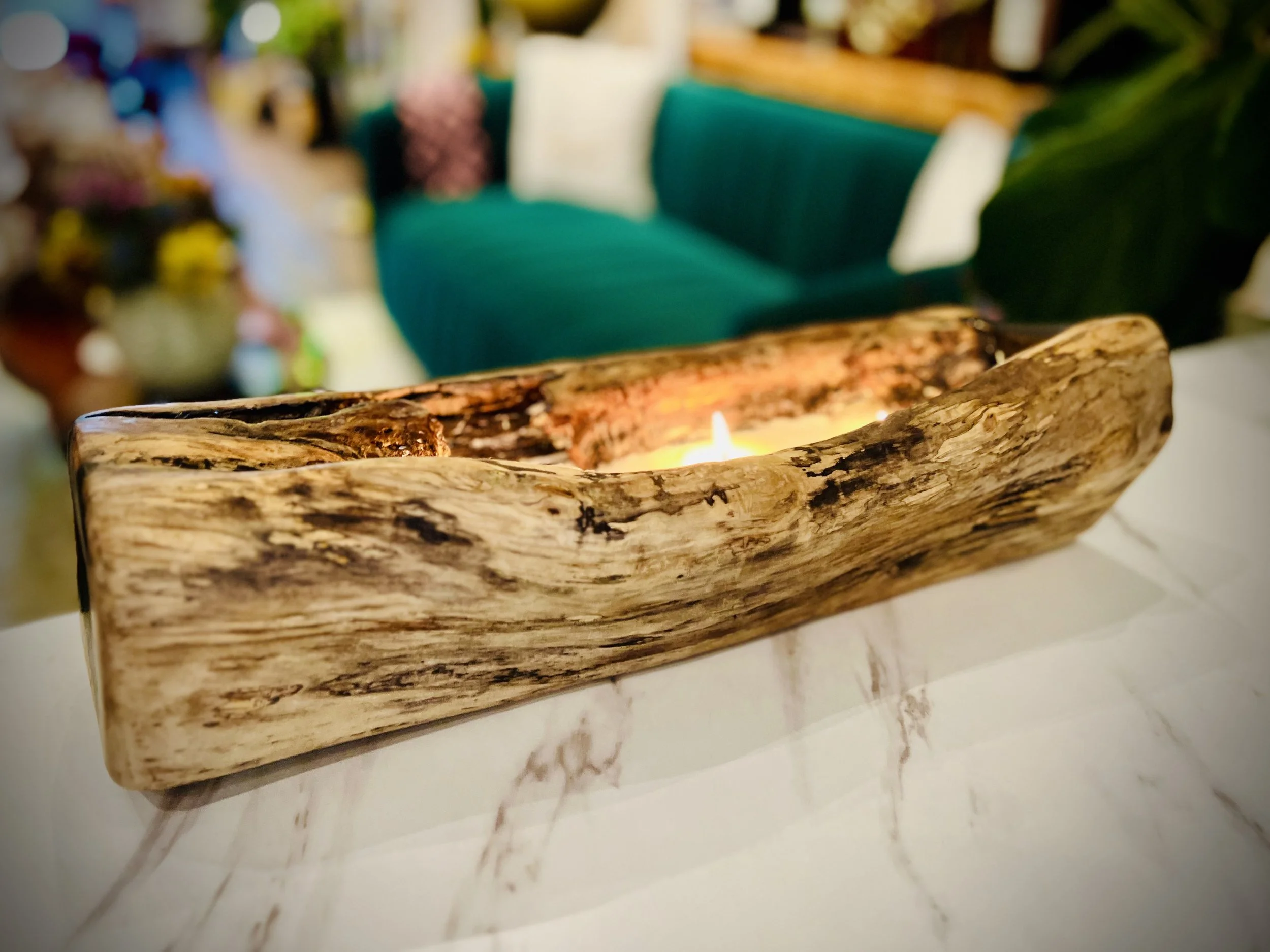 A rustic wooden candle holder with a small lit candle inside, placed on a white marble surface in a cozy indoor setting.