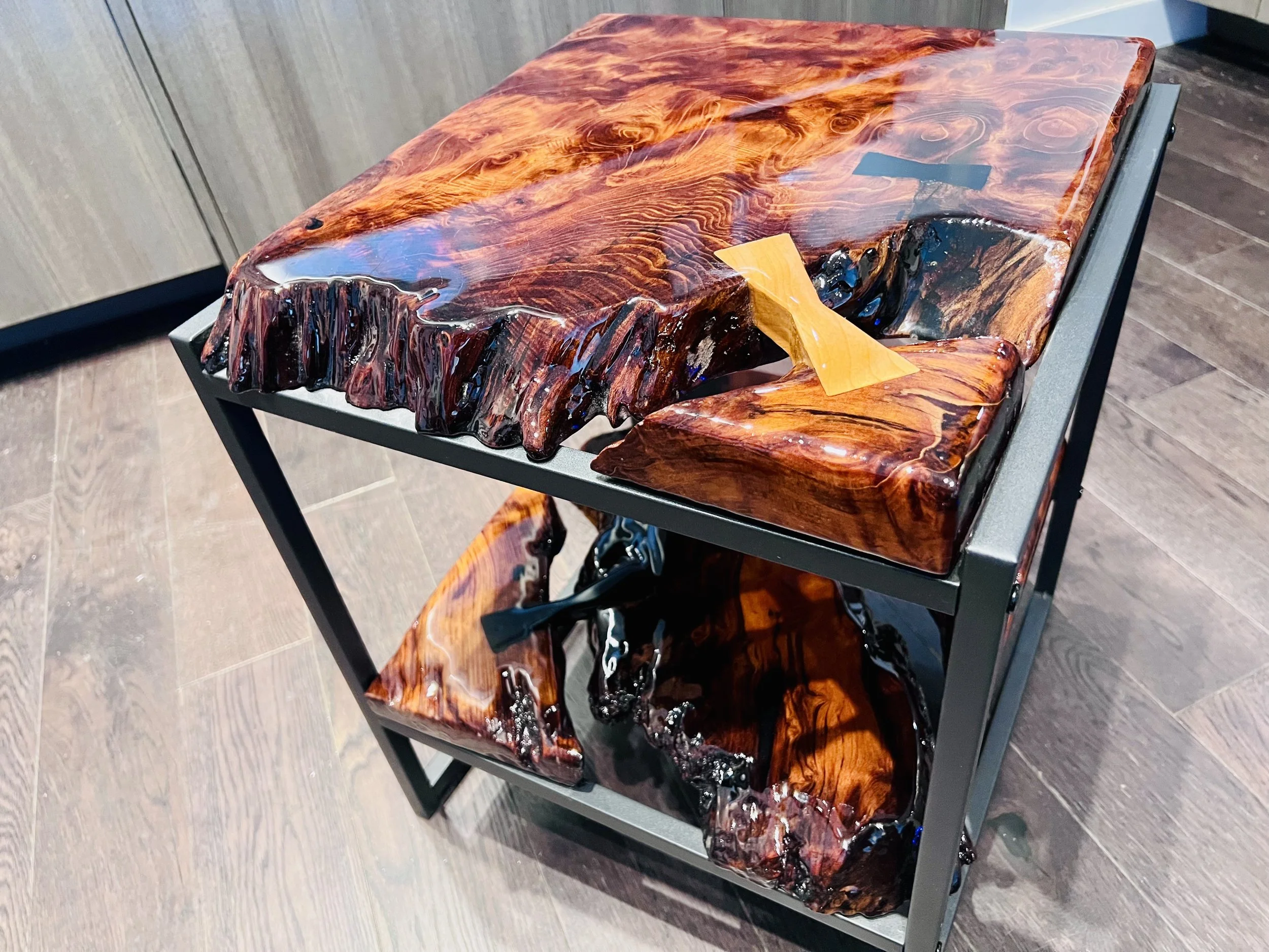 Wooden furniture with a polished, glossy surface showing a natural wood grain pattern, mounted on a black metal frame.