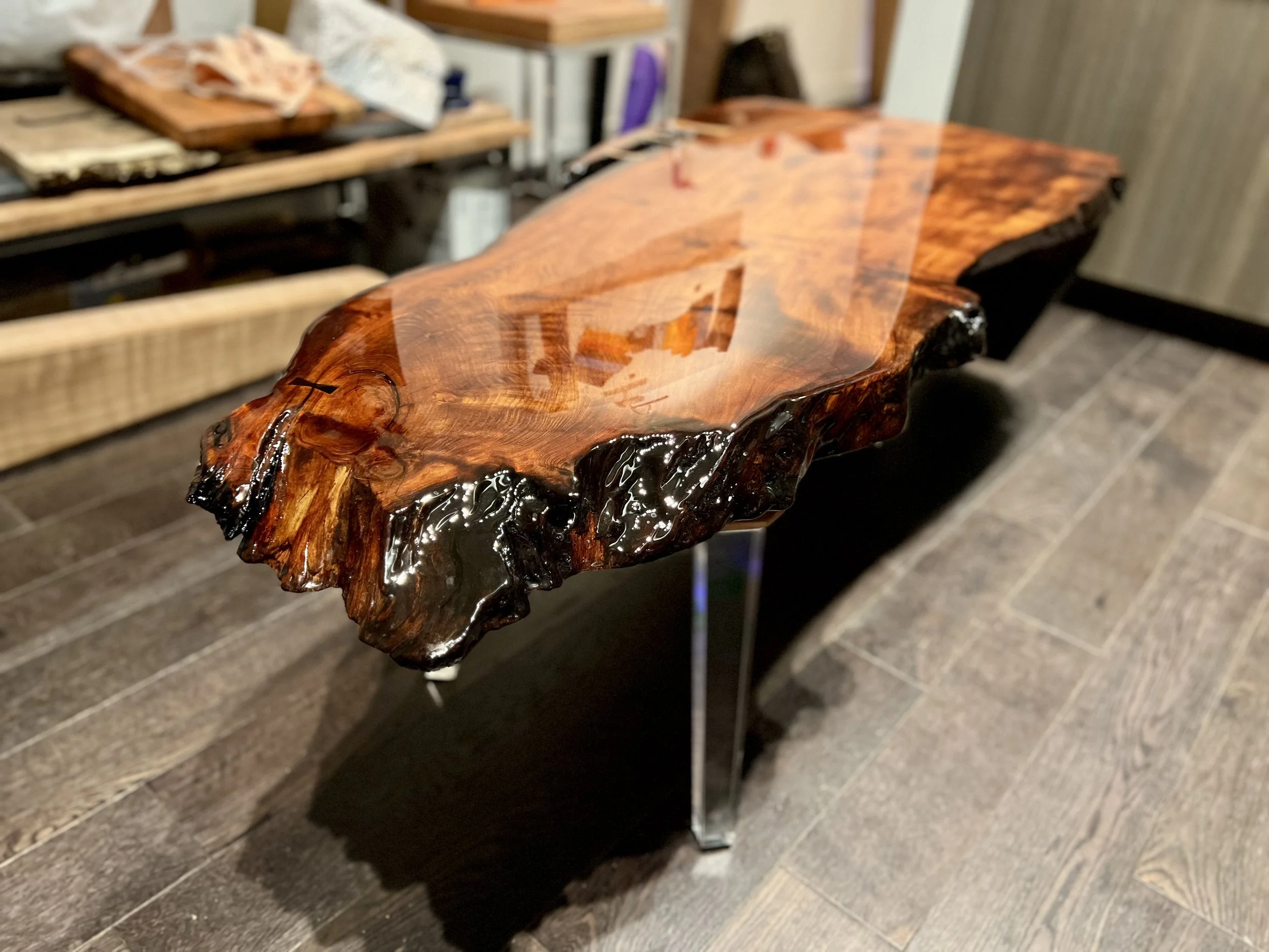 A polished wooden table with a natural edge, displaying a glossy surface that enhances the wood grain and color.