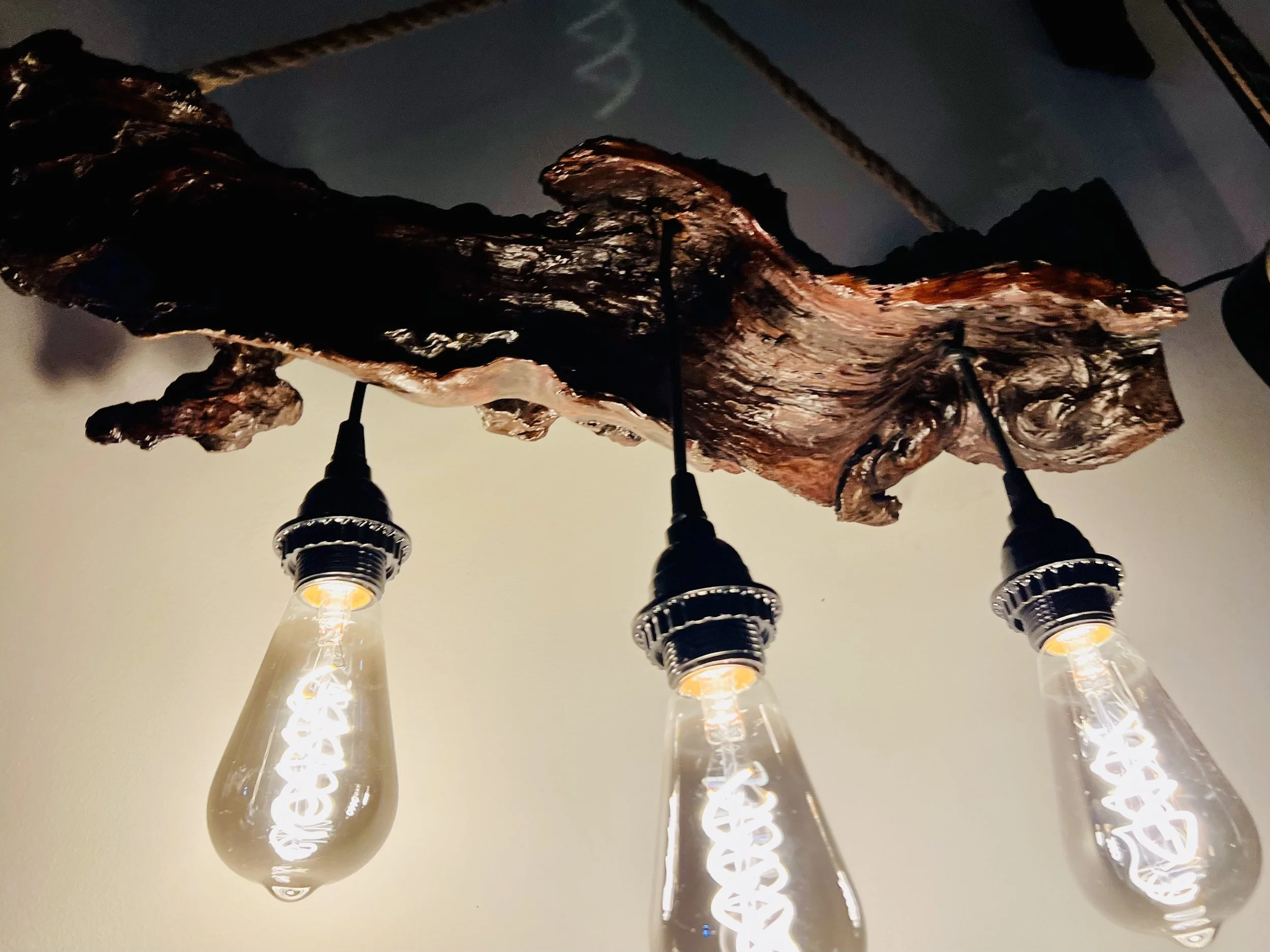 Close-up of a ceiling light fixture with three vintage-style Edison bulbs hanging from a piece of wood.