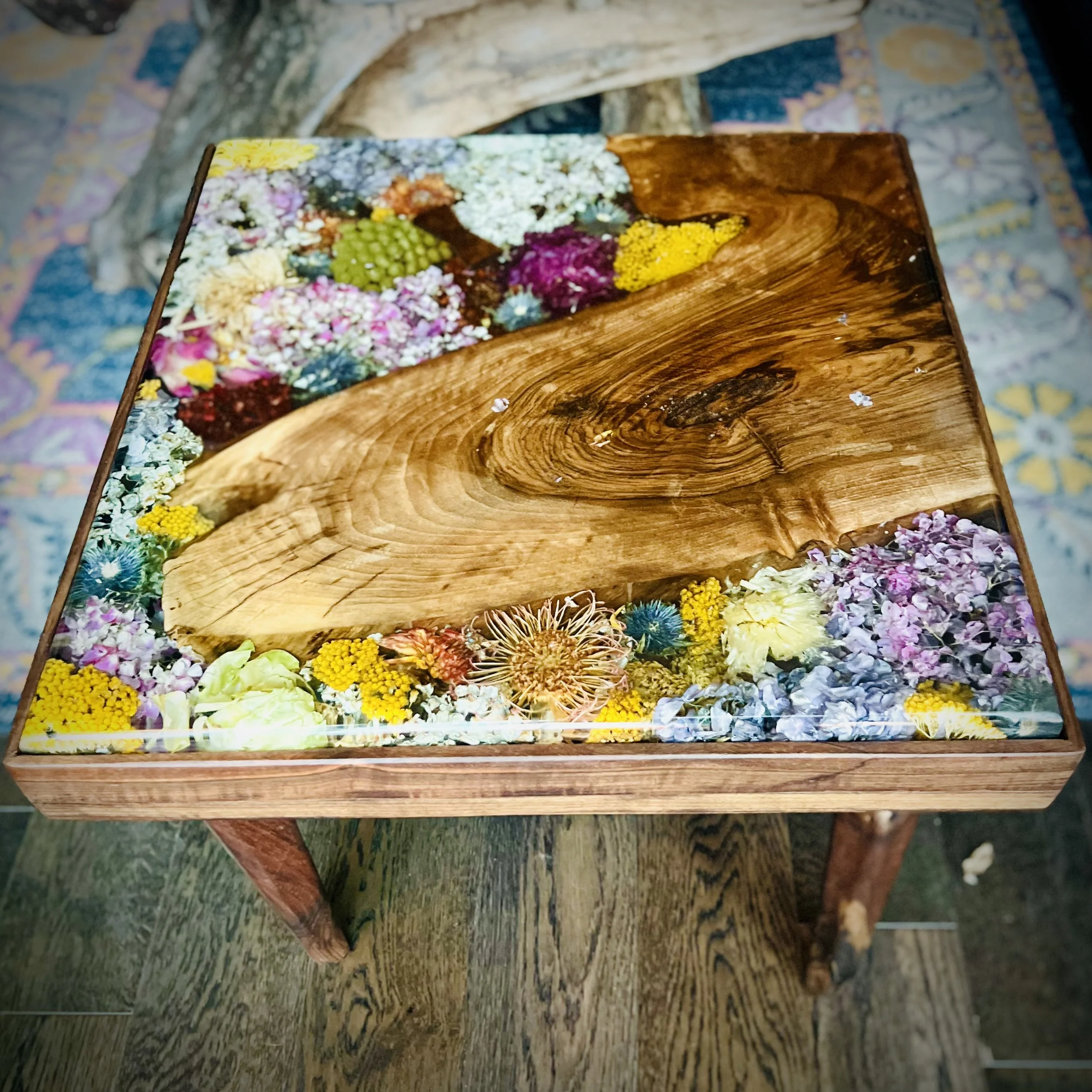 Wooden table with a glass top filled with colorful dried flowers and plant materials.