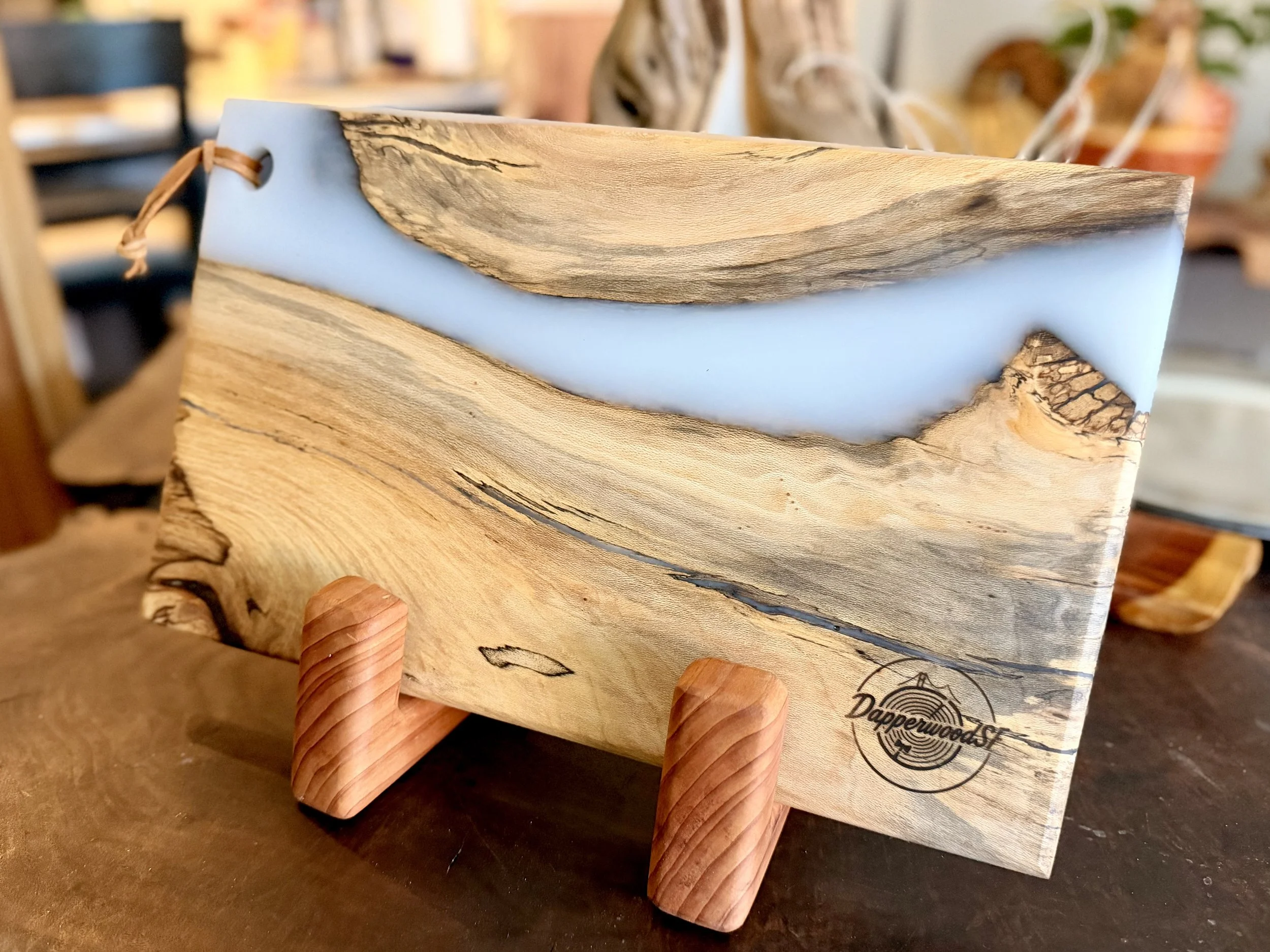 Wood and resin decorative piece on a small wooden stand, with a natural wood pattern and light blue resin inlay, branded with 'Dapperwoods'.