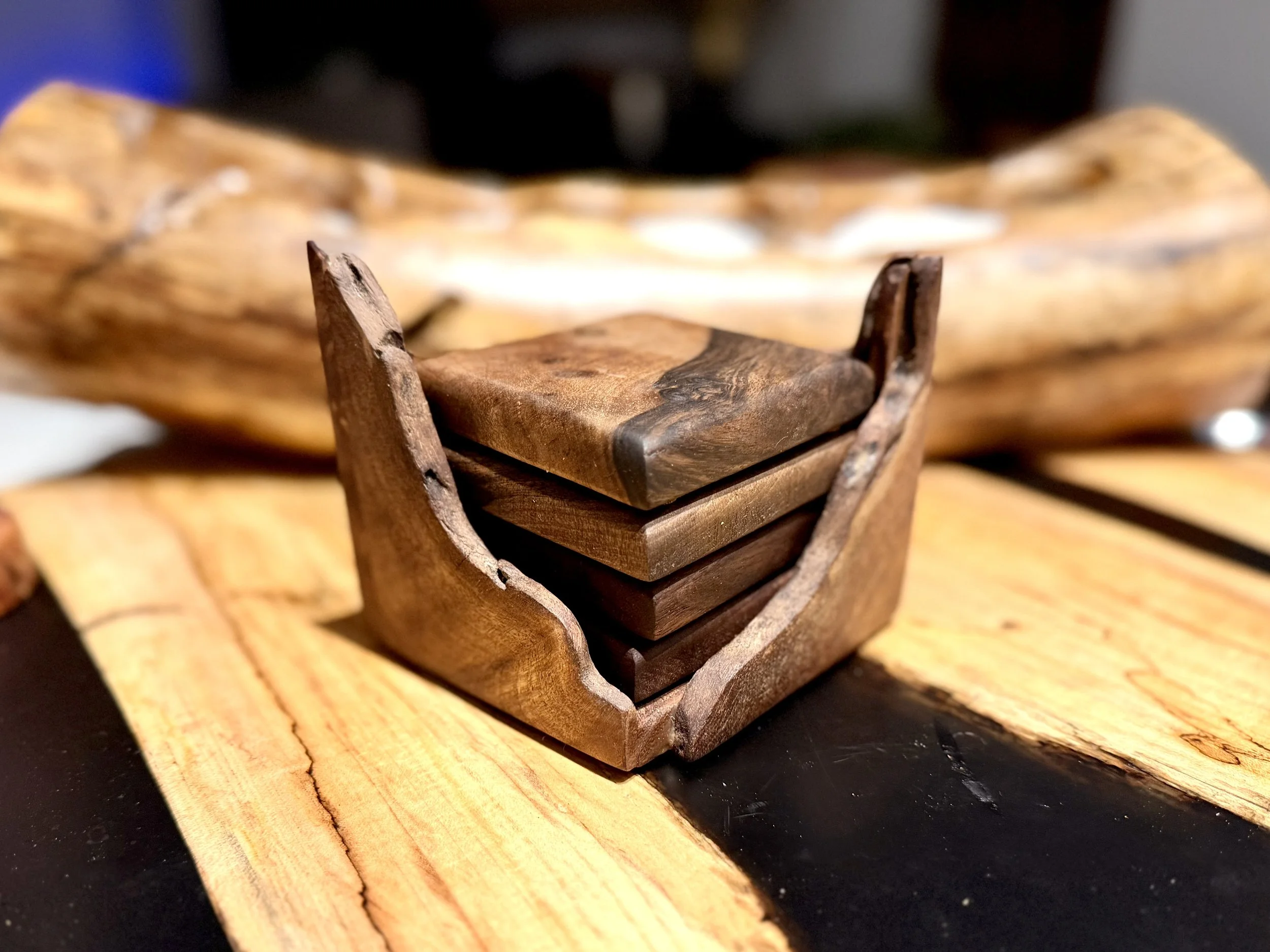 Close-up of a small wooden box with a lid, placed on a wooden surface. The box and surface are made of dark and light wood with natural grain patterns.