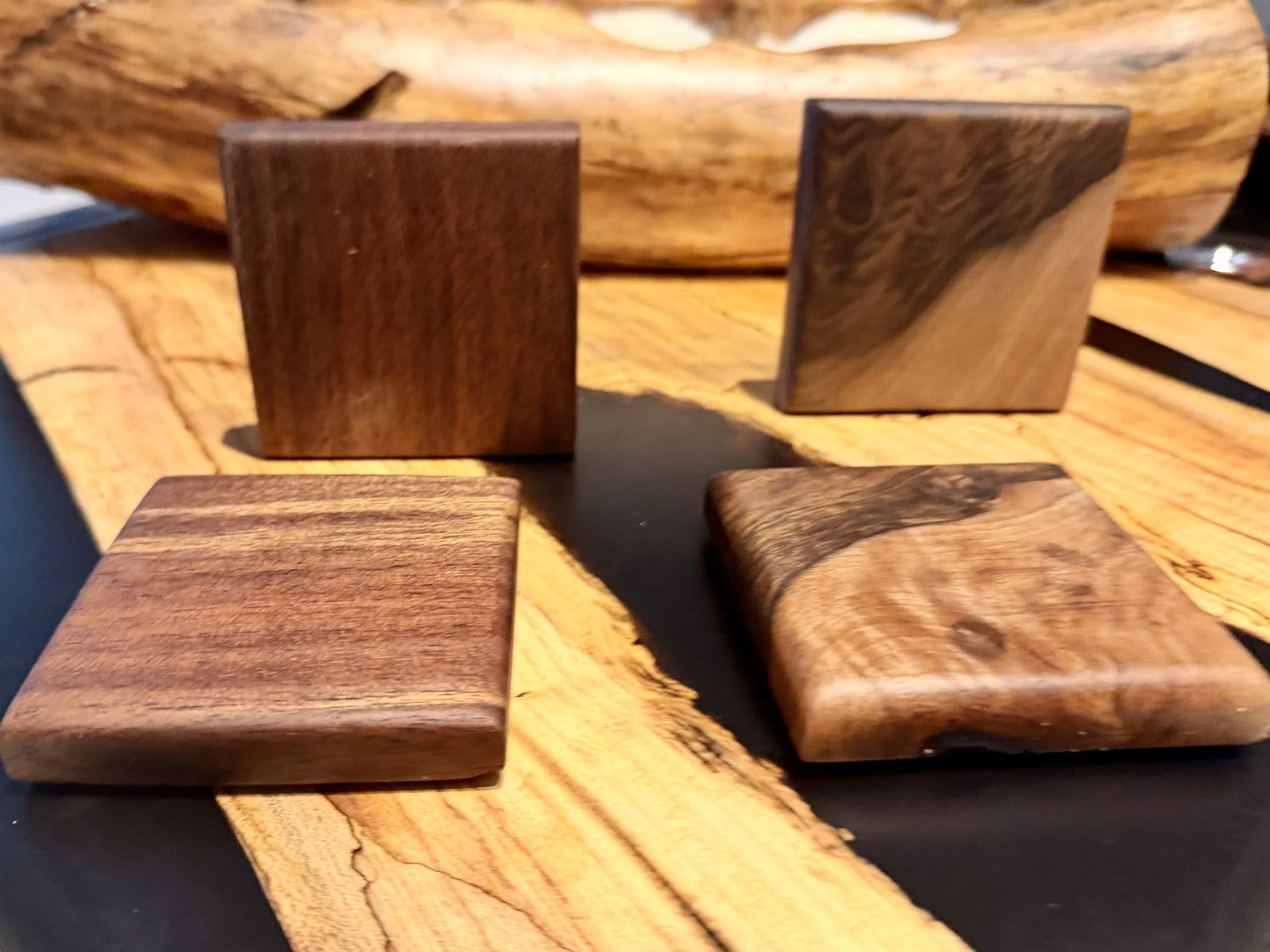 Four wooden blocks of different shapes and wood grains placed on a wooden and black surface.