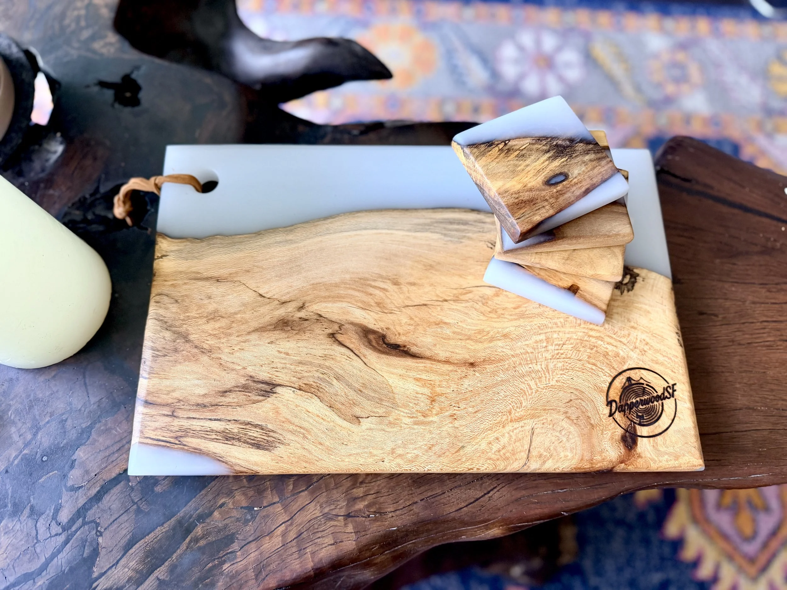 A wooden serving board with a stack of three bar of soaps, one with wood grain pattern and two with marble-like pattern, on a rustic wooden table.