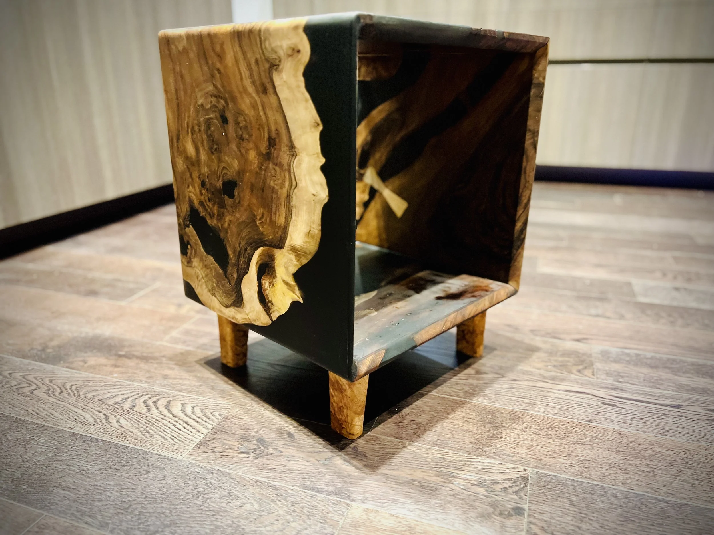 A small wooden and black metal cube-shaped table with four legs, sitting on a hardwood floor.