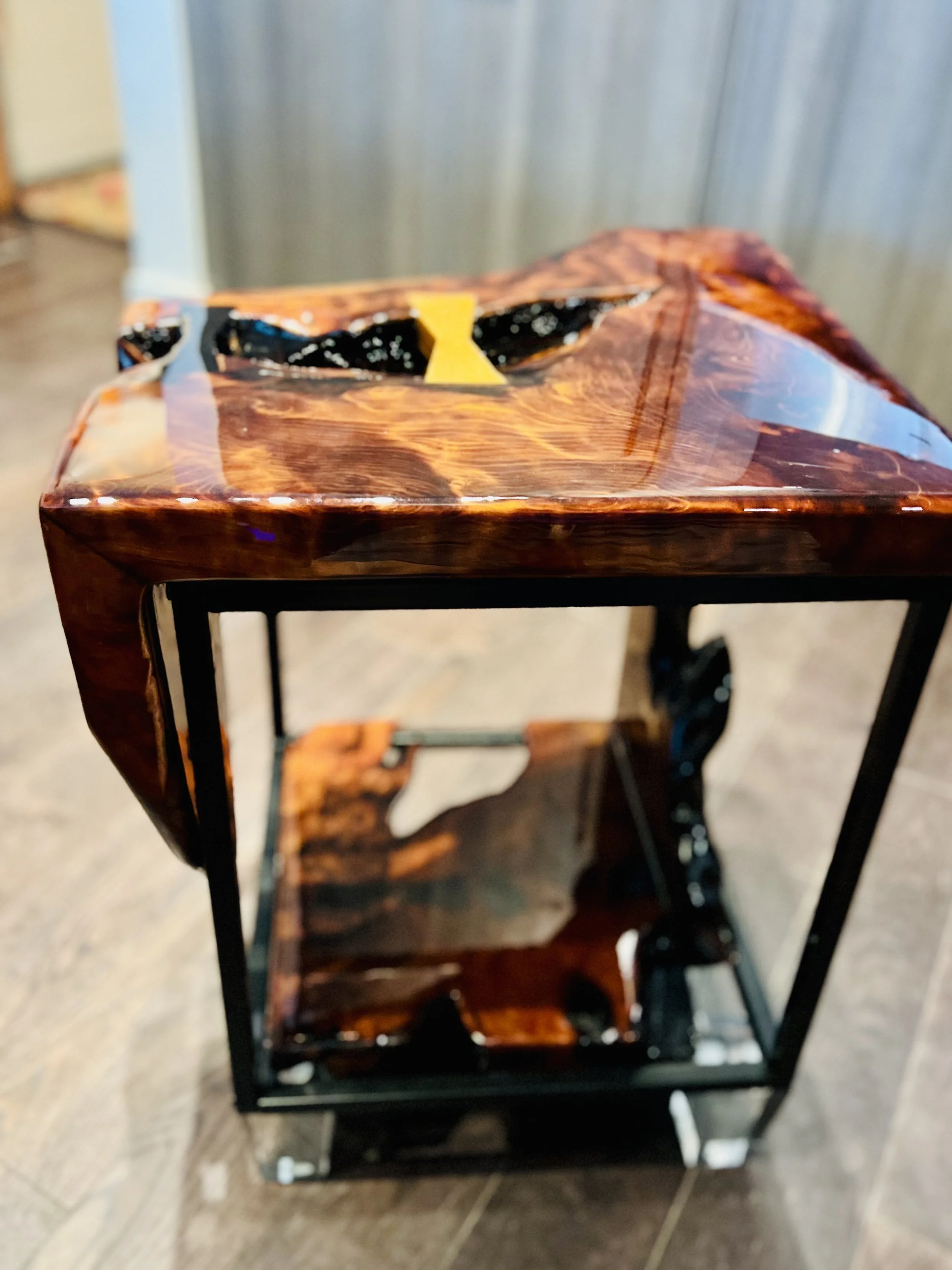 A small, decorative table with a wooden top and metal frame, featuring a cutout design of a face wearing sunglasses.