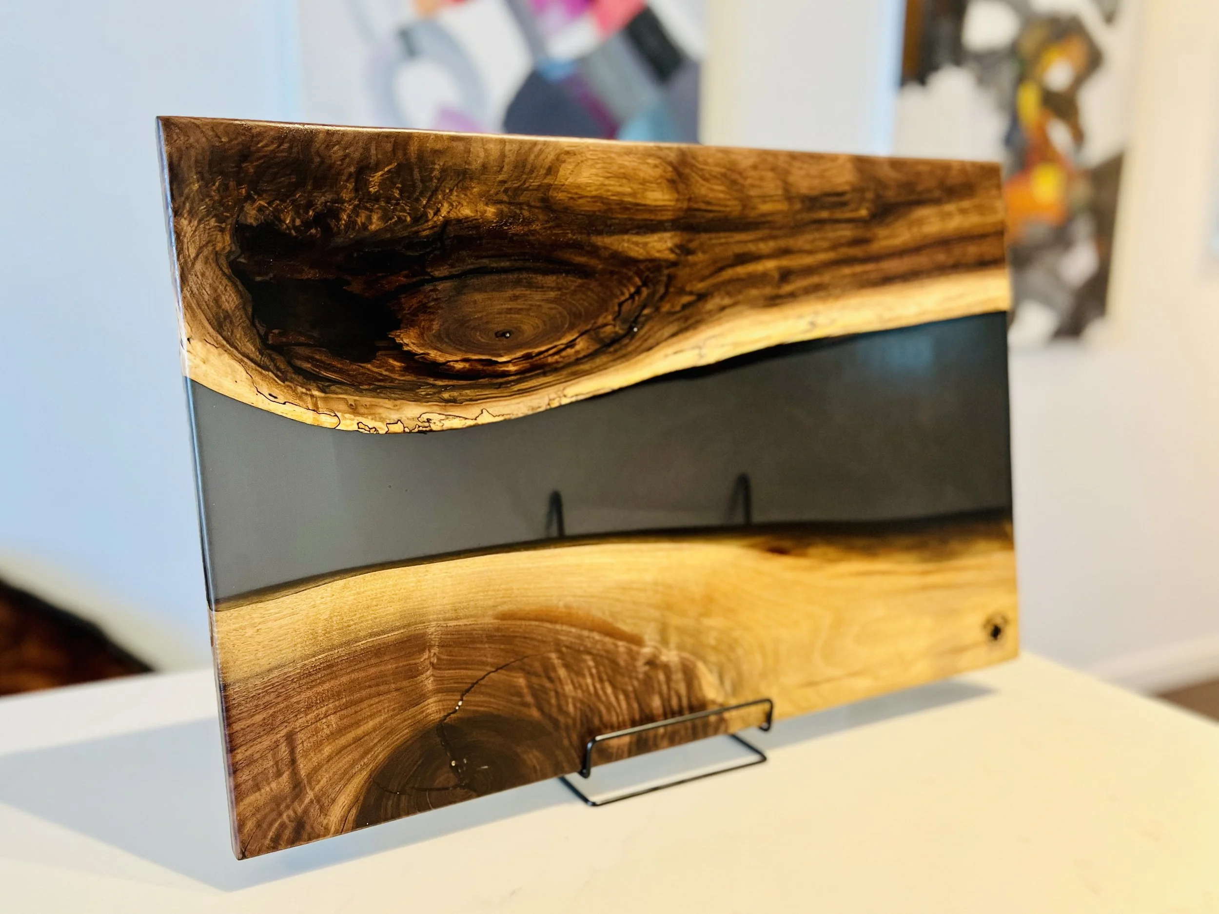 A decorative wooden and resin wall art piece on a stand. The top and bottom sections are natural wood with visible grain and knots, and a middle strip of smooth, gray resin.