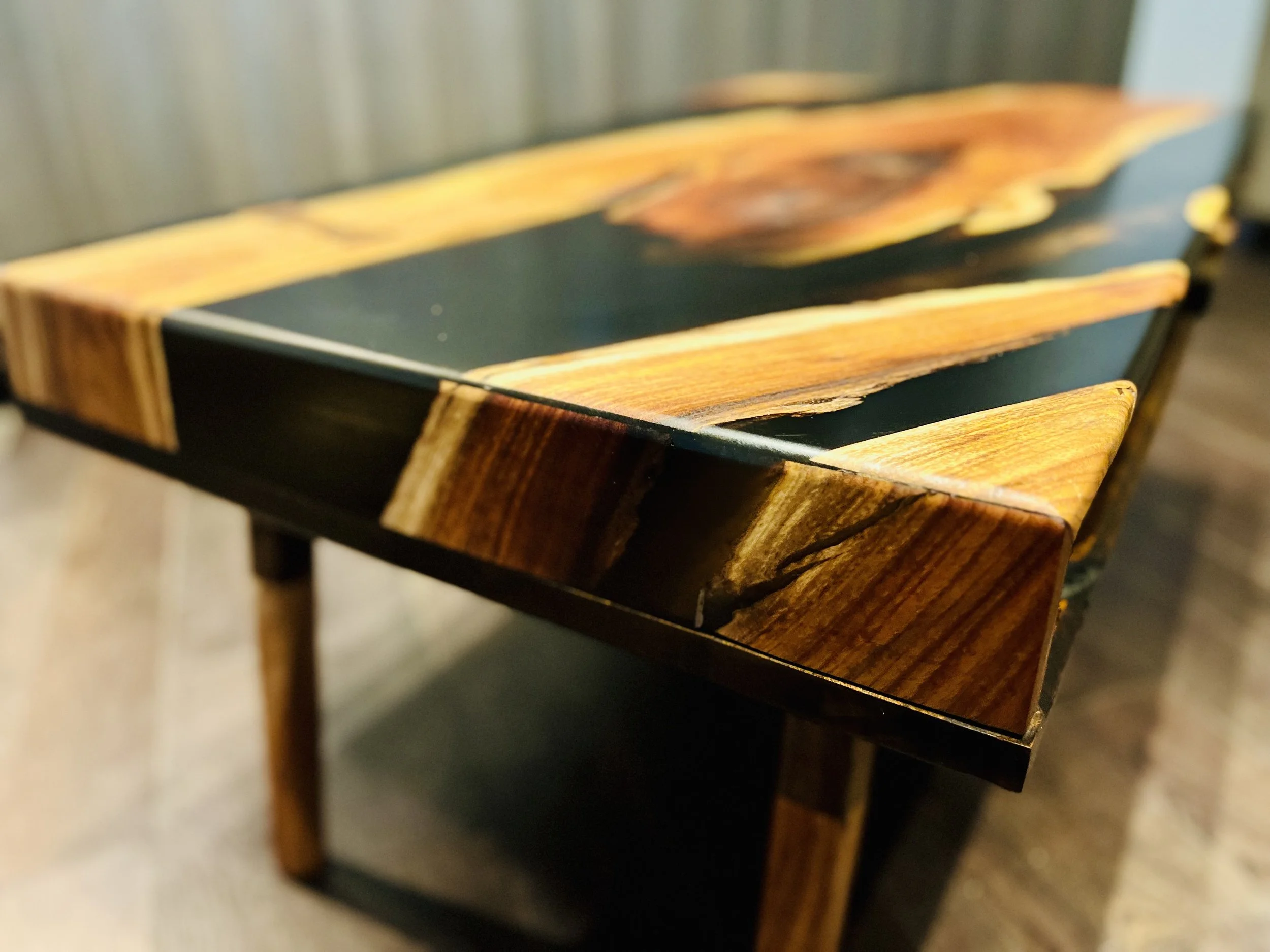 Close-up of a wooden table with a black top and decorative wood veneer edges, featuring different shades of brown and orange.