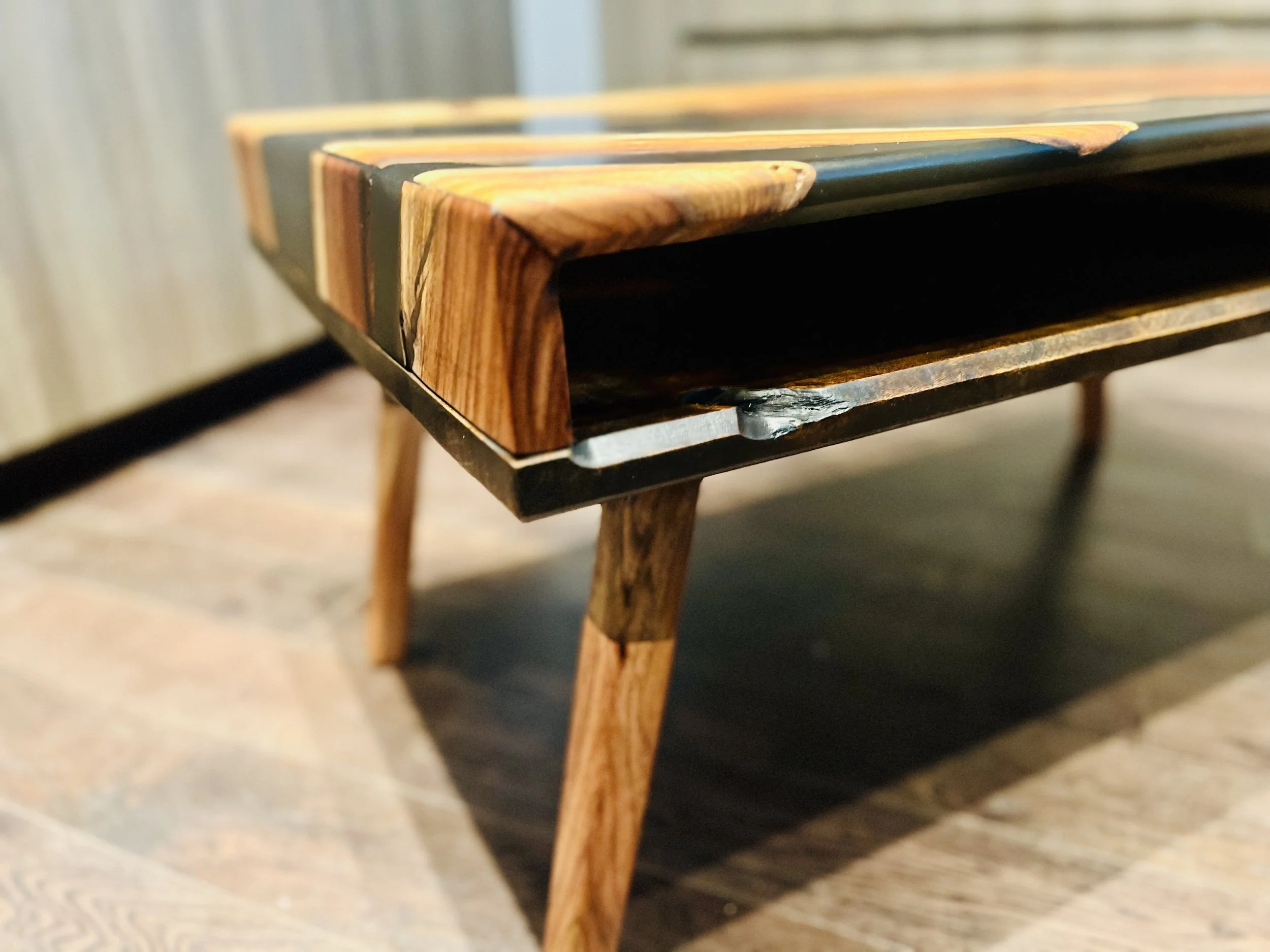 Close-up of a wooden coffee table with a black metal frame and tapered wooden legs.