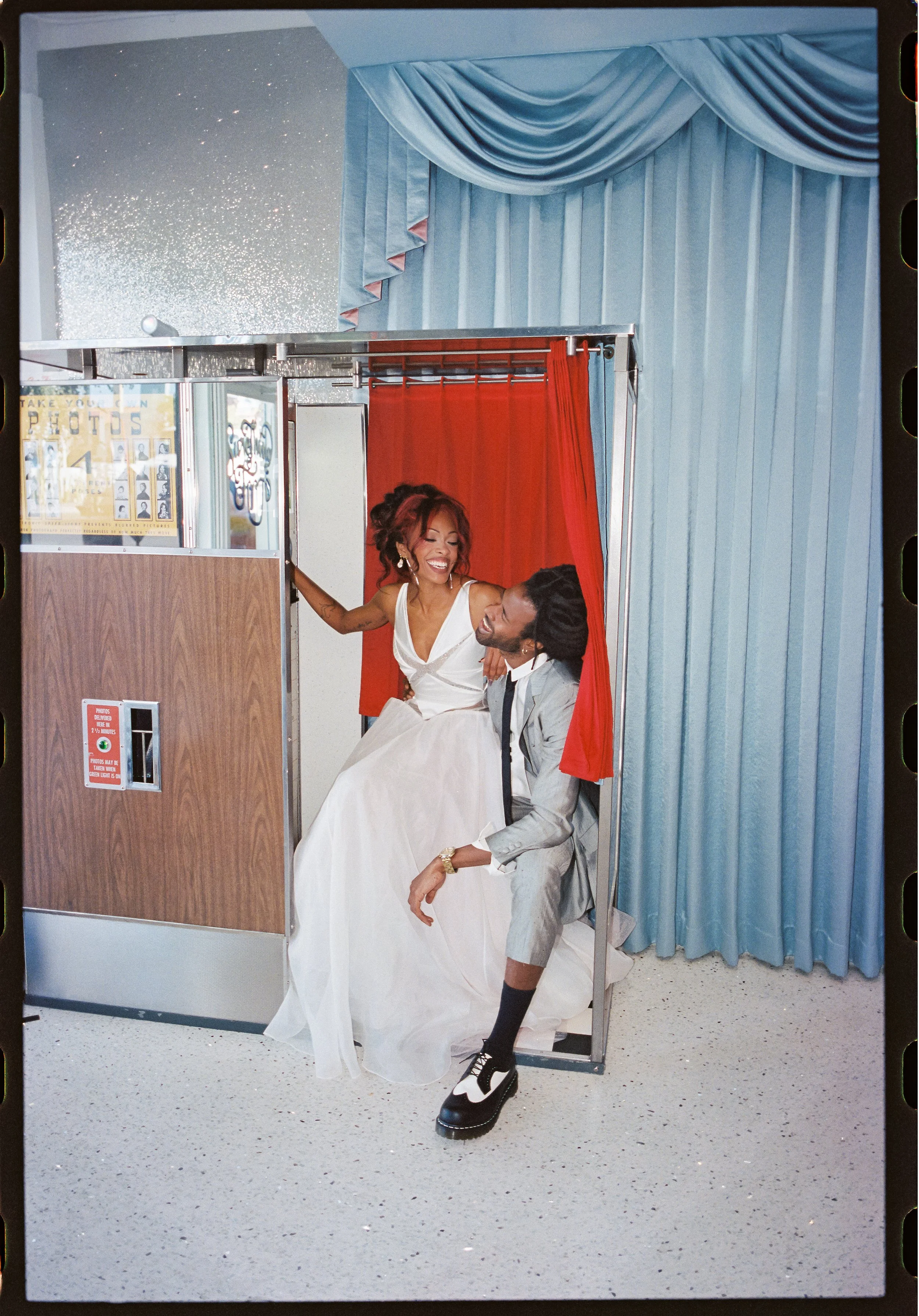 photo of cool stylish alt couple laughing in a vintage photobooth at sure thing chapel in las vegas, nevada