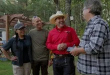 Four people share a laugh outdoors, including a man wearing a red shirt, cream cowboy hat and colourful woven sash.