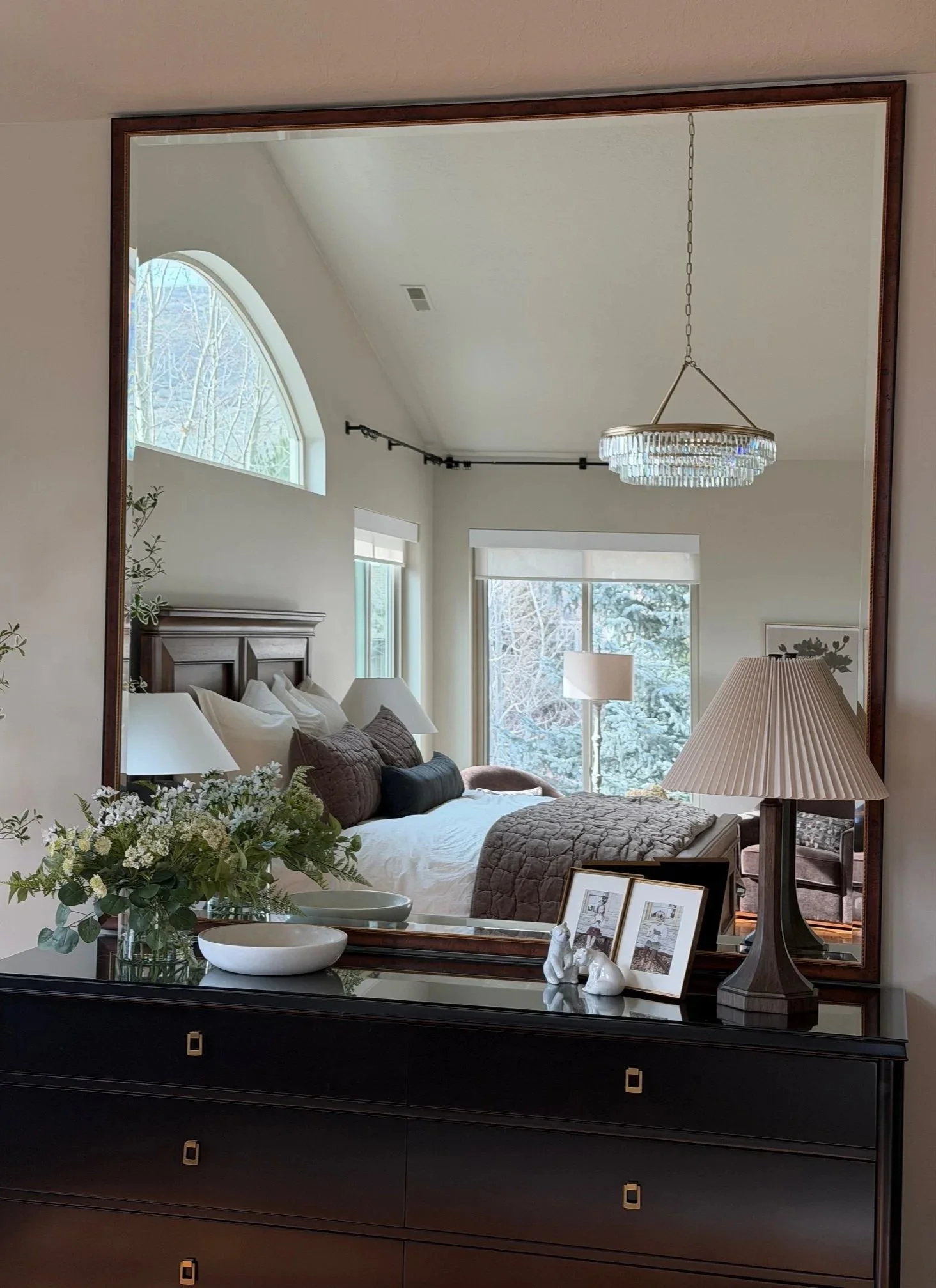 A bedroom with white walls, a bed with white and gray bedding, framed artwork above the bed, two small white bedside tables with lamps, a sliding barn door, and a view into a bathroom with a bathtub.