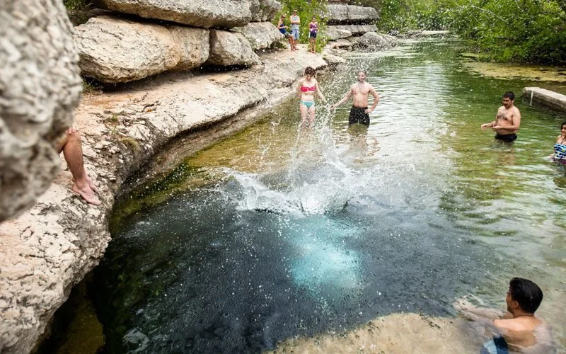 People swimming and relaxing in a natural water hole surrounded by rocks and trees