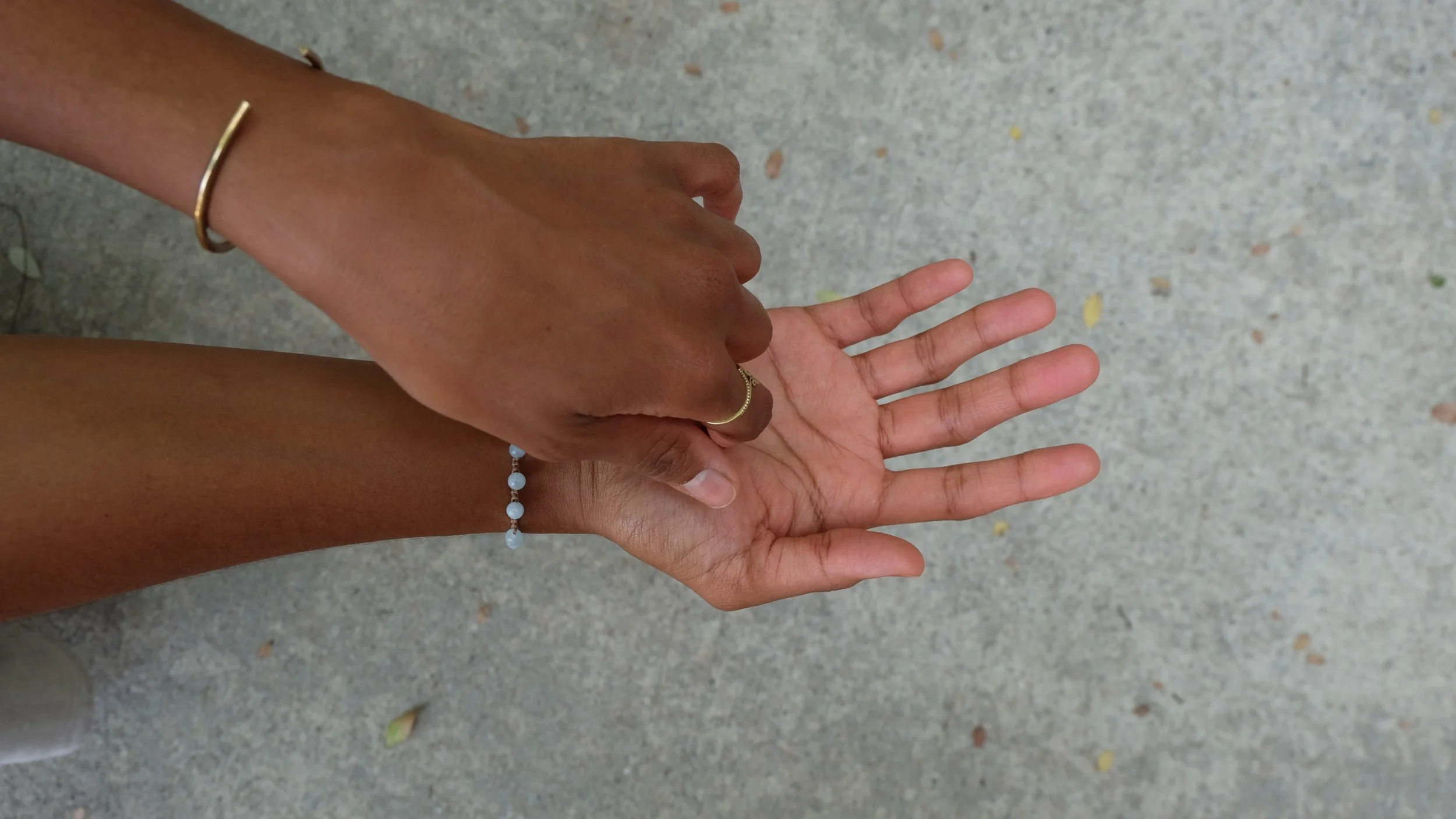 Two hands, one with darker skin and one with lighter skin, touching or holding each other outdoors on a concrete surface.