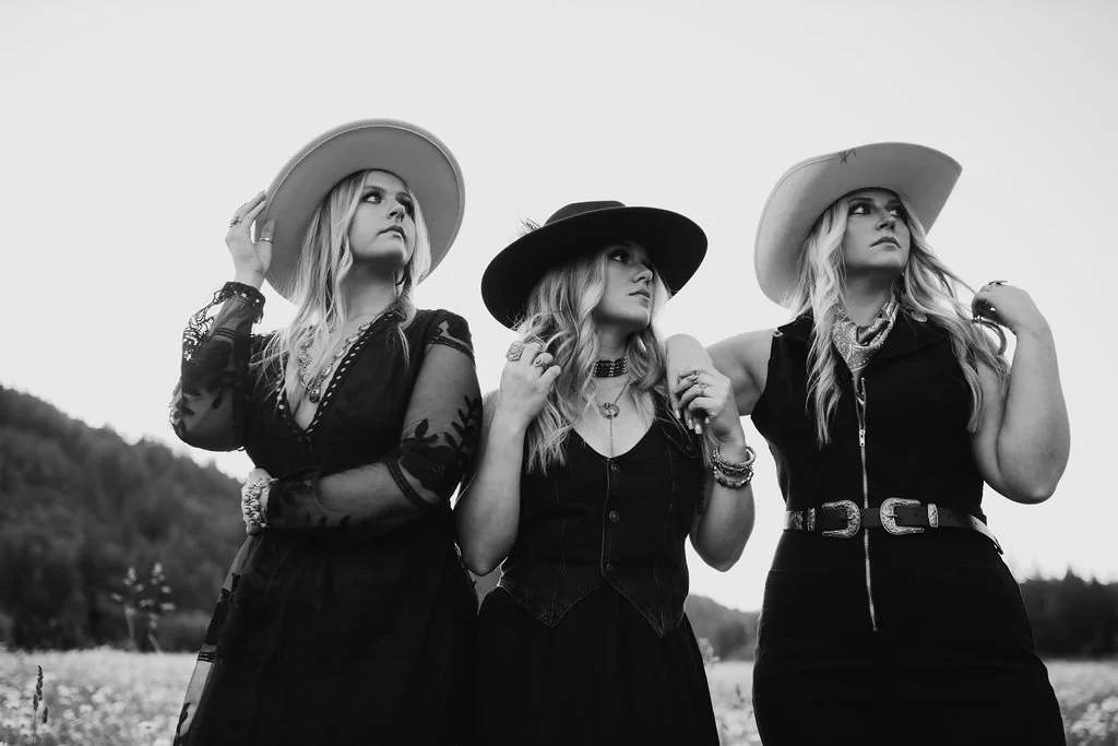 Three women with long hair wearing western-inspired hats and outfits