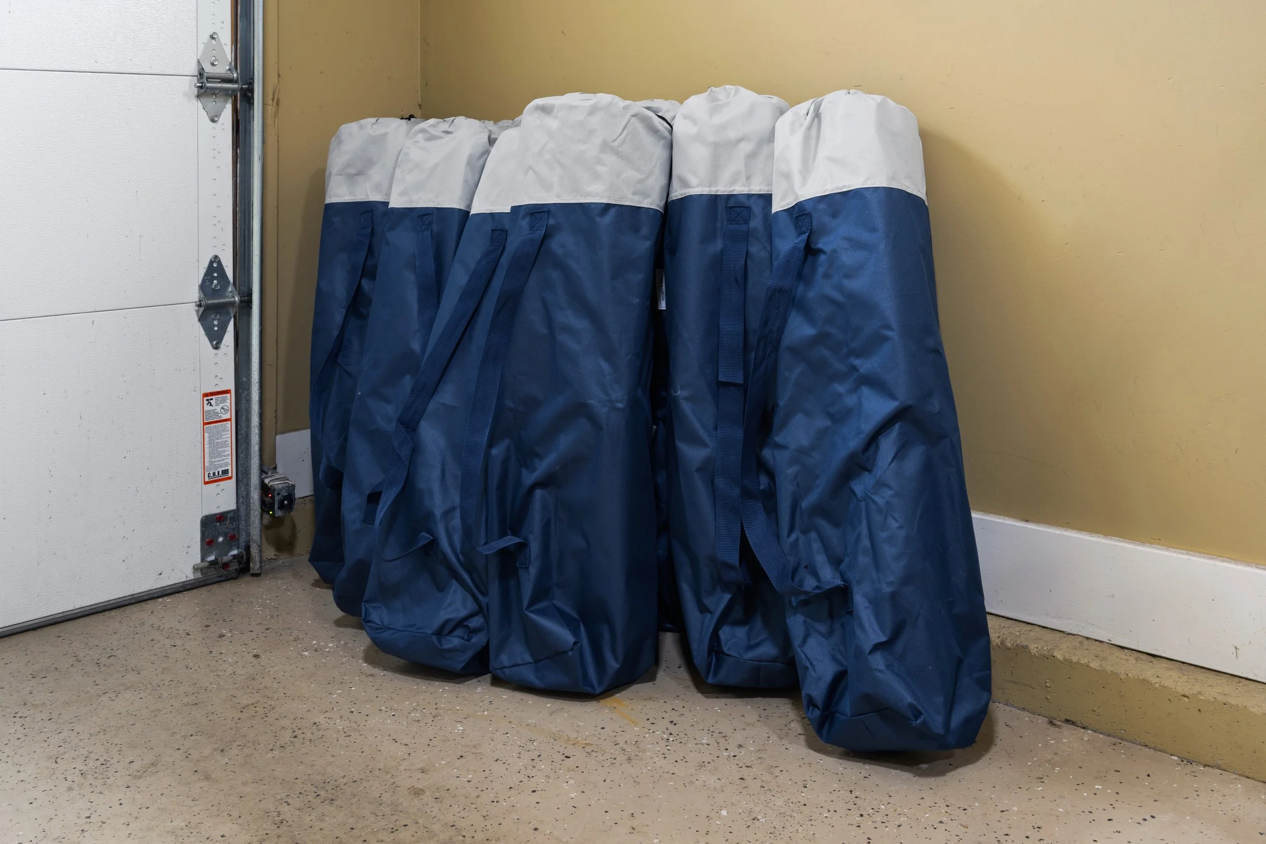Multiple large blue and white bags lined up next to a corner in what appears to be a garage or storage room.